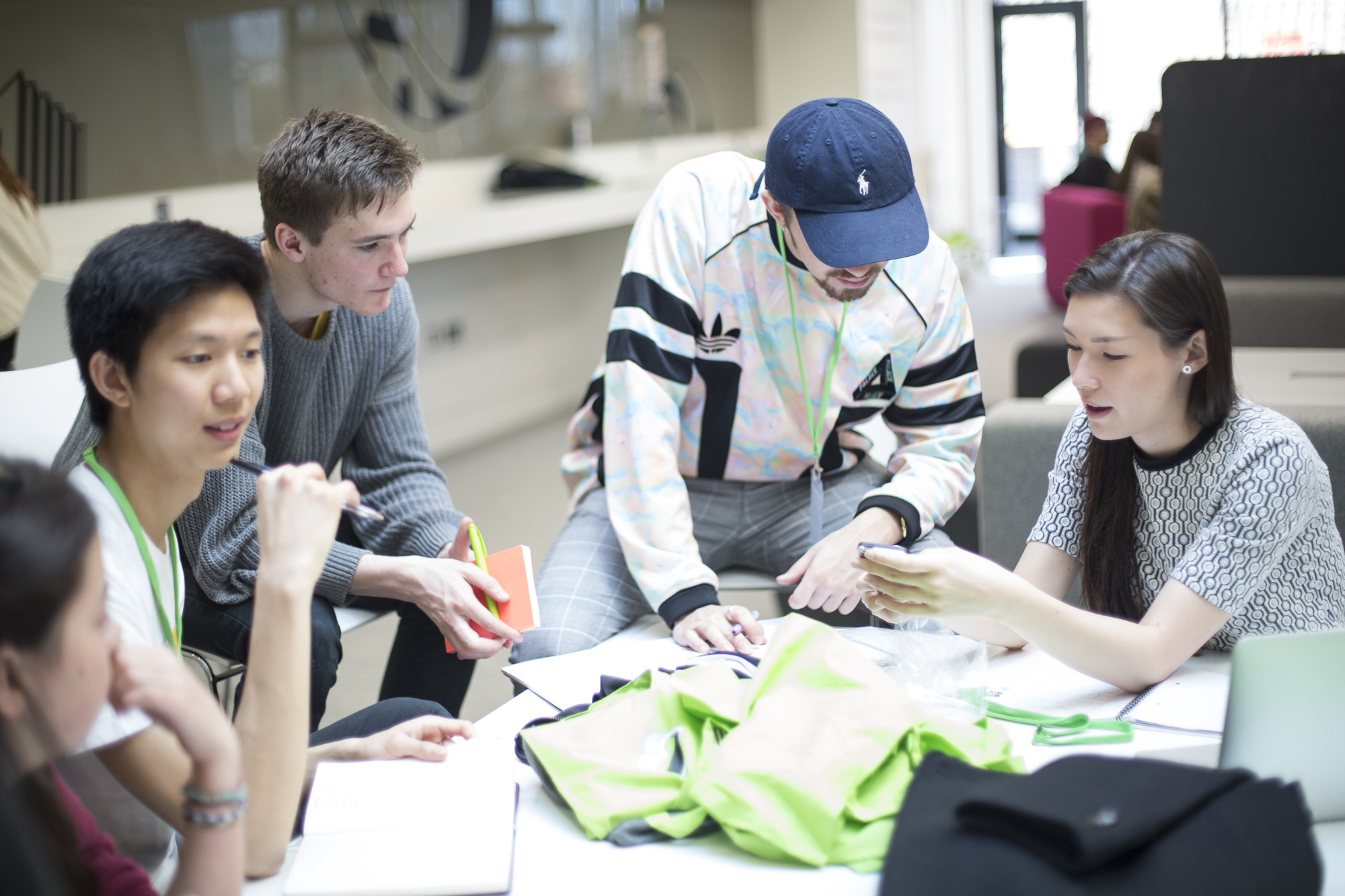 Five students sat around a table. One is showing another something on their phone.