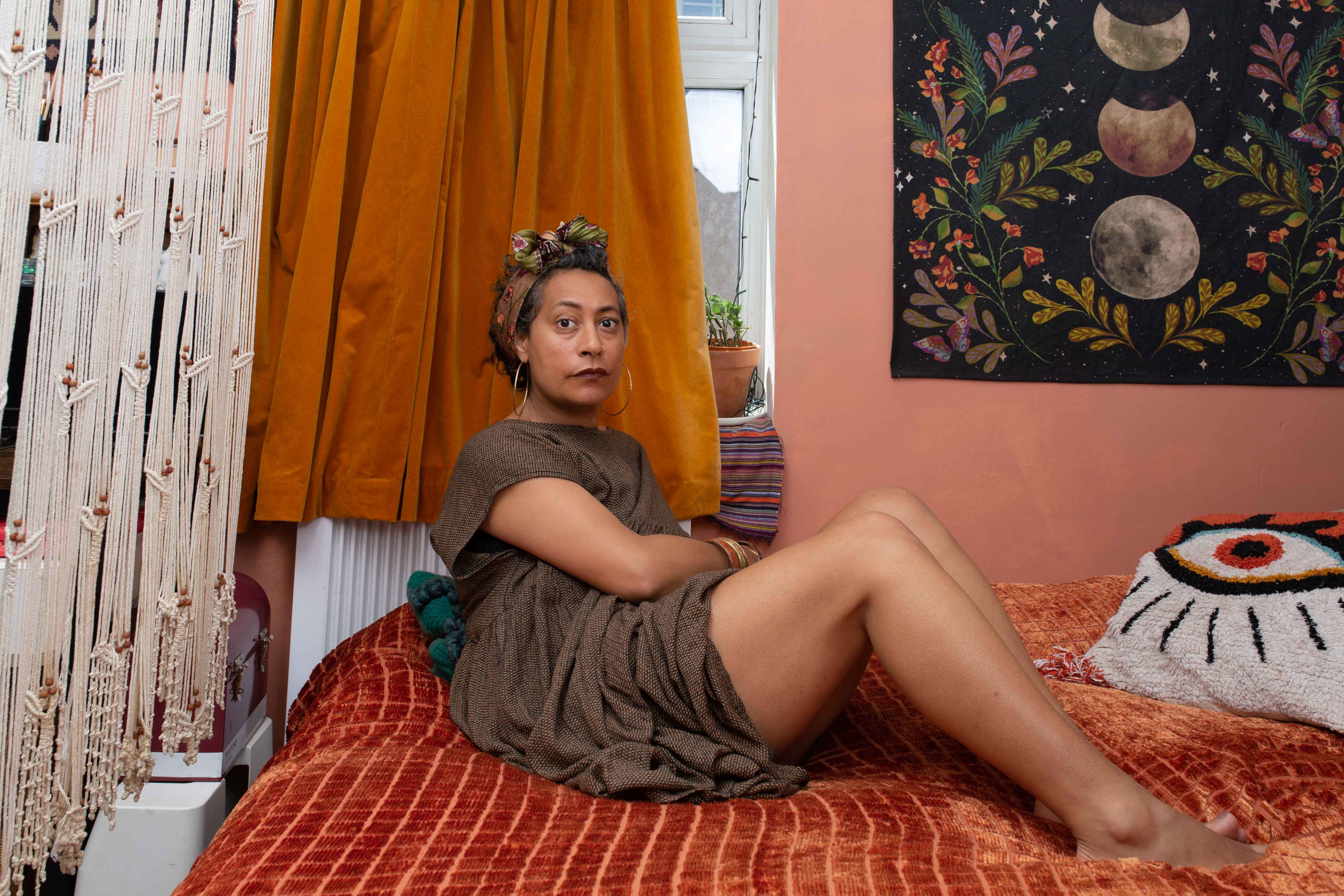 A woman posing for a photo on a bed, a curtain drawn behind their head.
