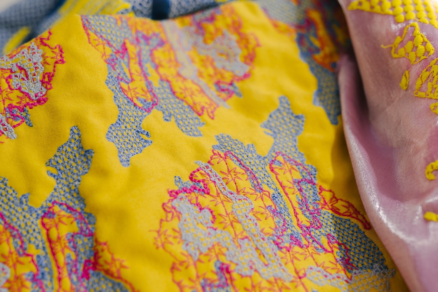 Bright yellow fabric with intricate paisley patterns in pink, orange, and blue. Adjacent pink textile visible with similar ornate designs.