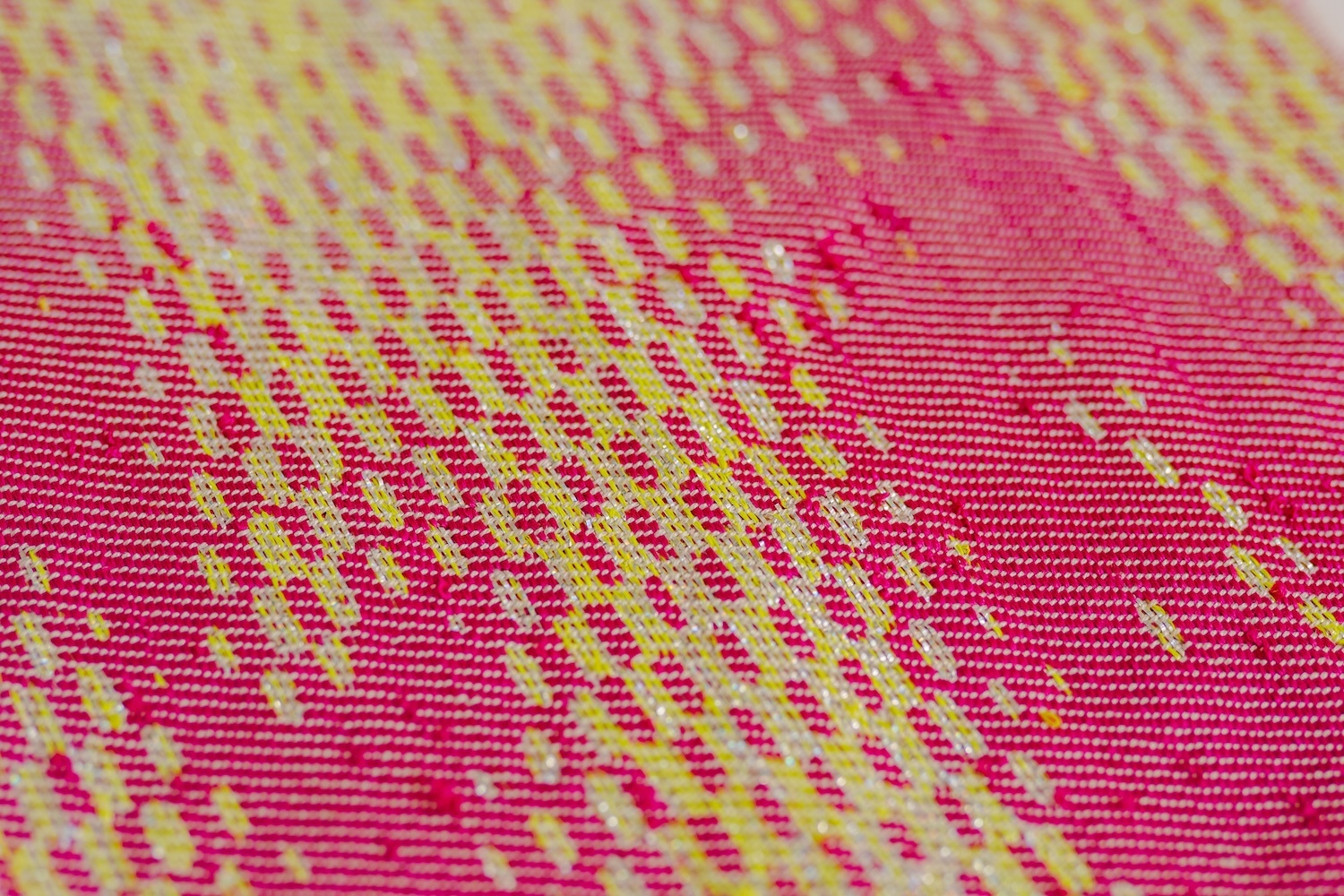 Close-up of woven fabric with pink and yellow threads creating diagonal geometric patterns across the textile surface.
