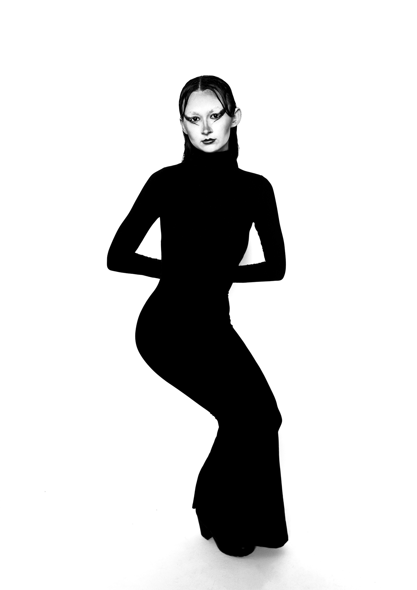 A model wearing a form-fitting black turtleneck dress strikes a pose against a white background. The model has styled hair and makeup that contrasts sharply with the outfit.