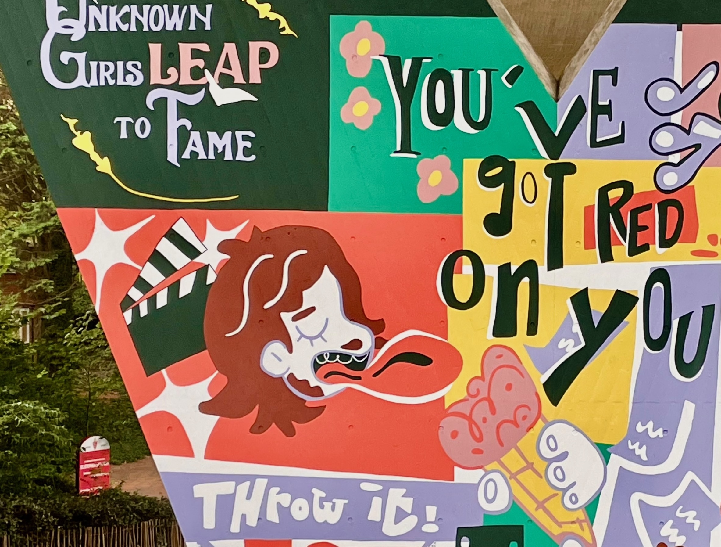 Part of a mural on a flyover pillar wall. Illustrations on multicoloured backgrounds showing the side profile of a man's face with his mouth open and tongue extended towards an ice cream, a clapper board behind him. Text reading "You've got red on you" appears on the right-hand side.