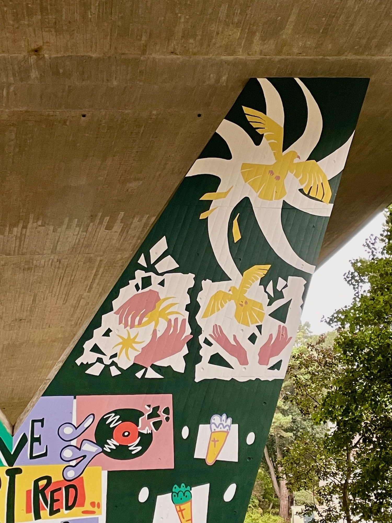 Part of a mural on a flyover pillar wall. Three images showing a pair of hands with yellow star-like shapes, then the same hands opening to release a yellow bird, and the yellow bird flying away.