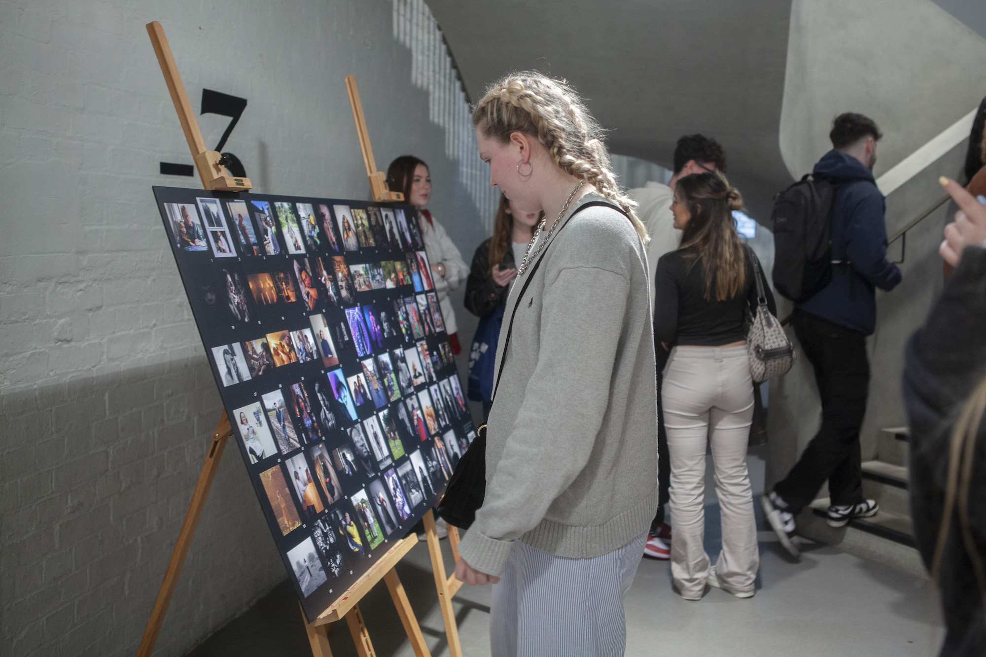 A person looking at a collection of photos on a black background held up by two easels, art exhibition.