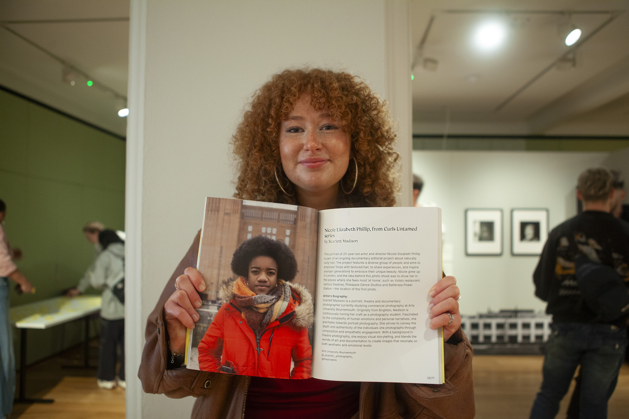 A person with frizzy hair holding open a photography book in an exhibition.