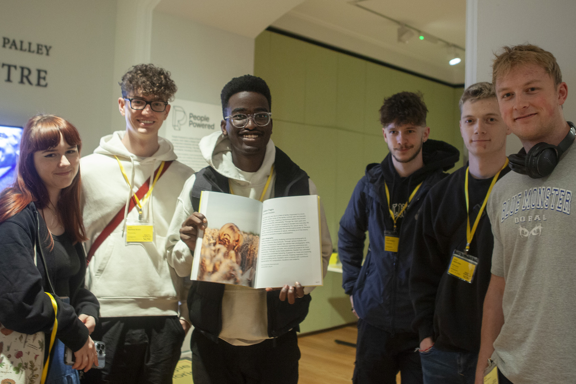 A collection of students at an exhibition, the middle one holding open a photography book.