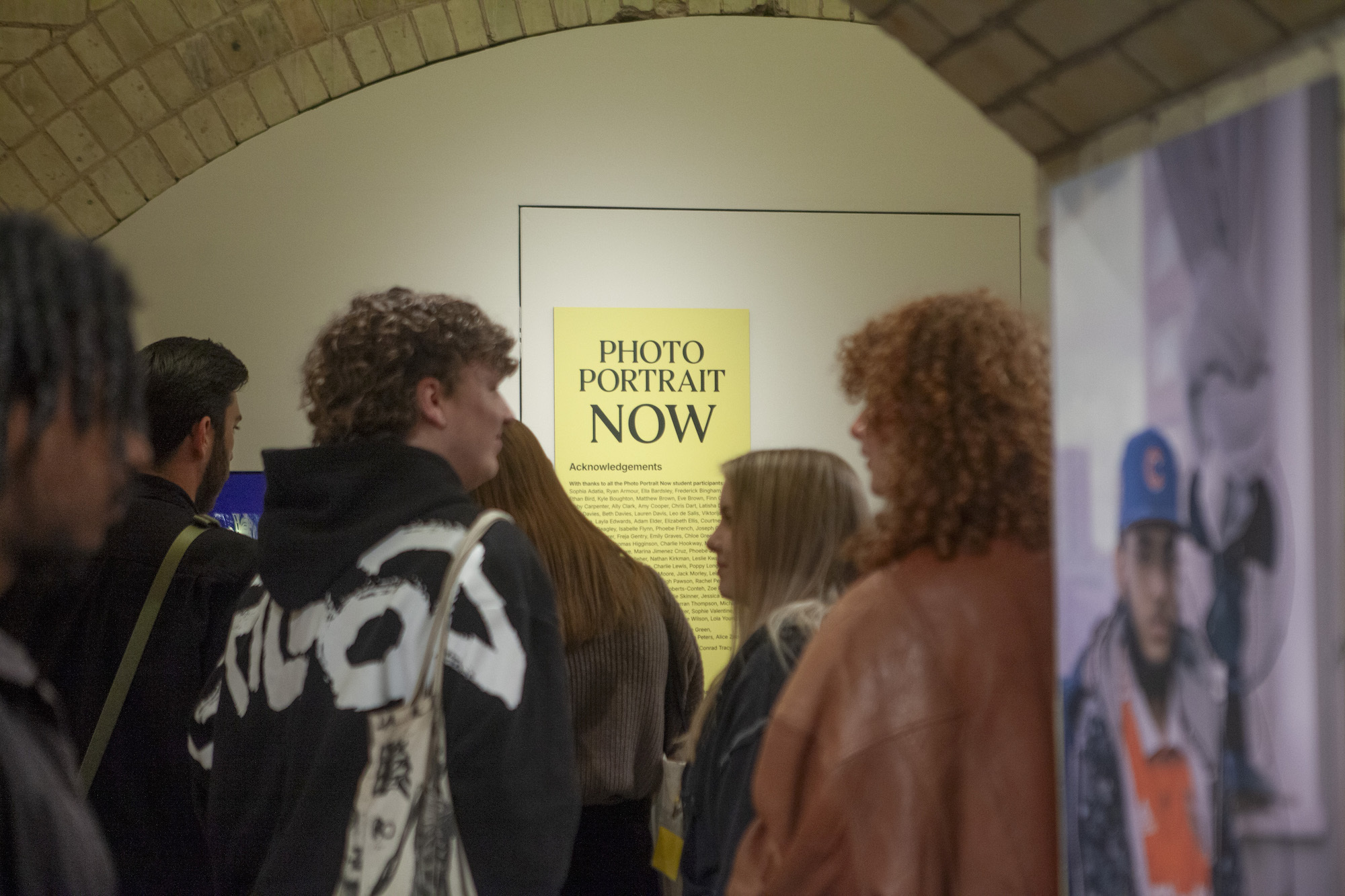 A group of people in a hallway with a yellow poster in the background that reads 'Photo Portrait Now'.