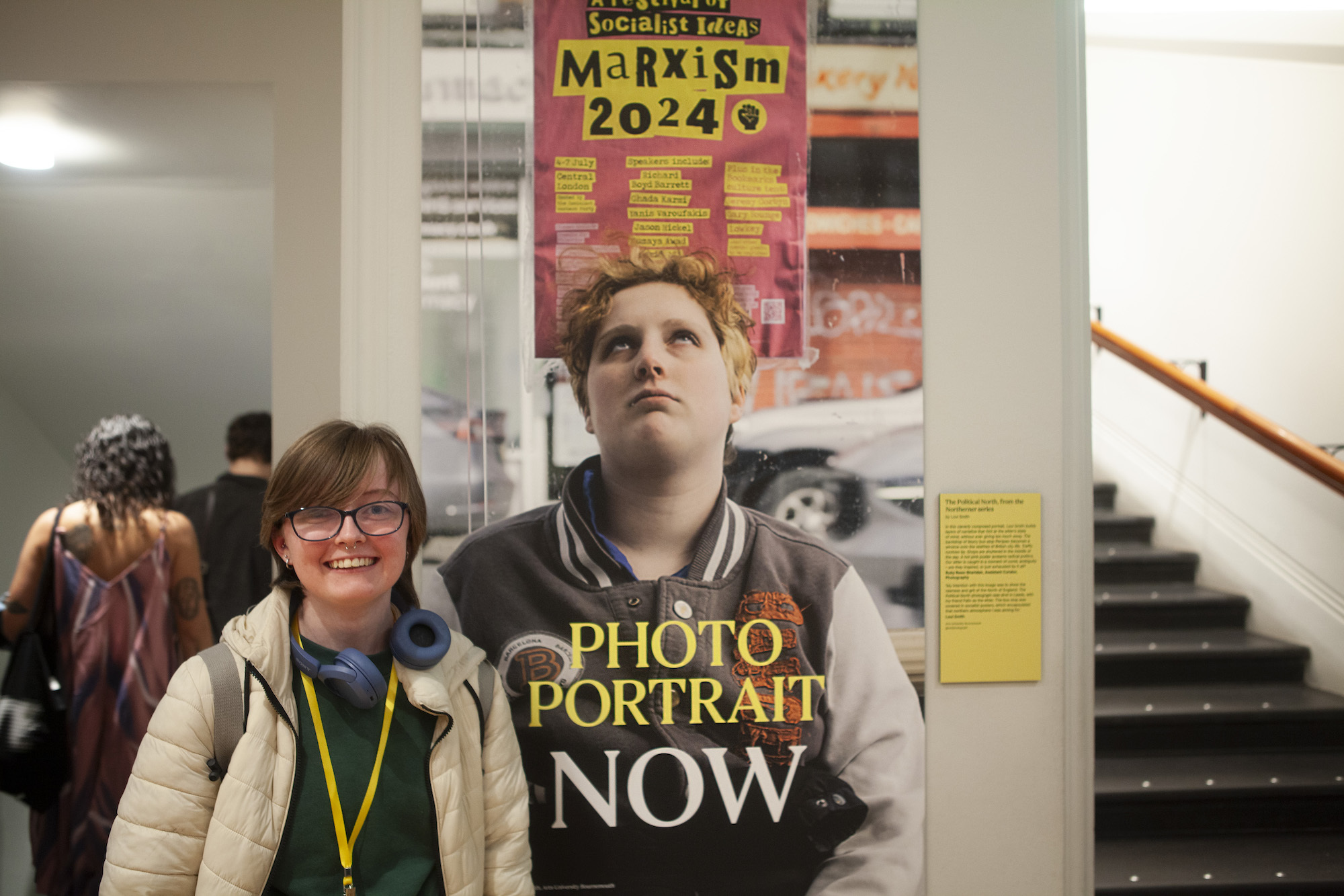 A person stood in a hallway by a poster of a person looking up at a poster, title reads 'Photo Portrait Now'.