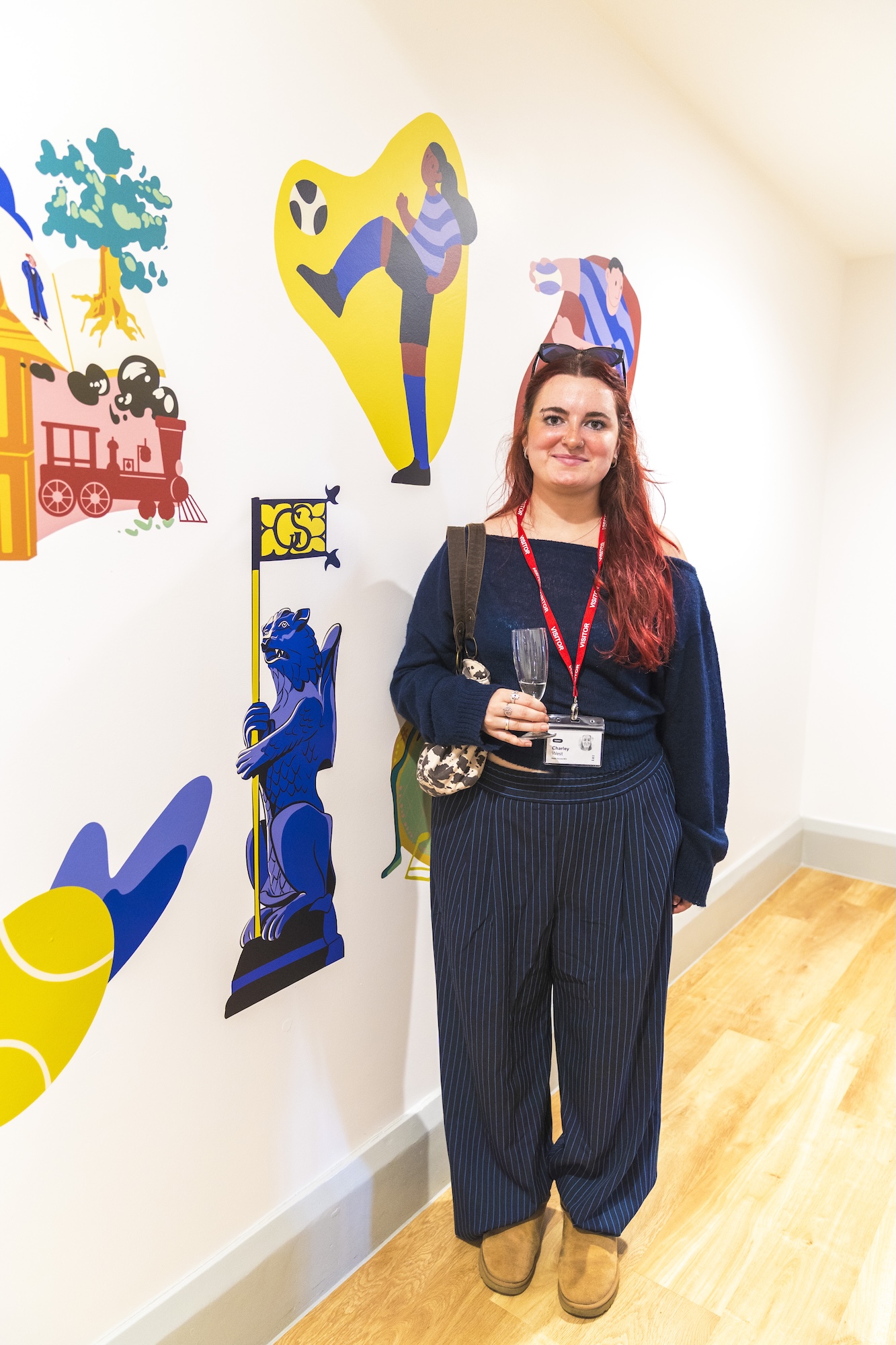 BA (Hons) Illustration student C West posing for a photo next to four vibrant vinyl illustrations on the wall next to them.