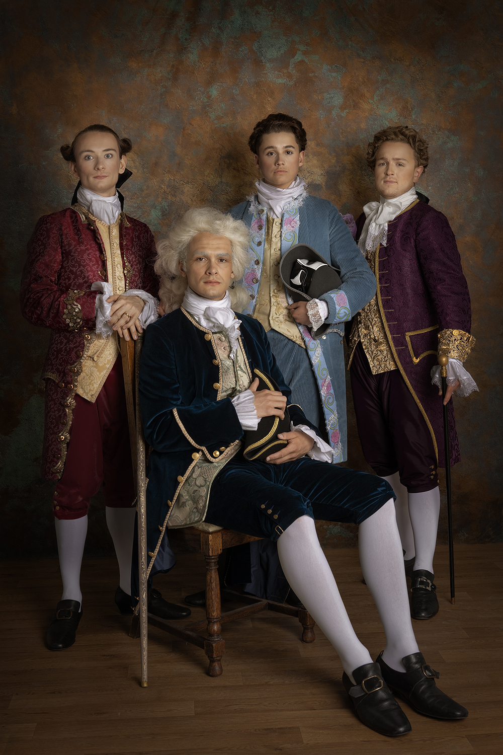 Four men dressed in 18th century menswear, one sat and three standing