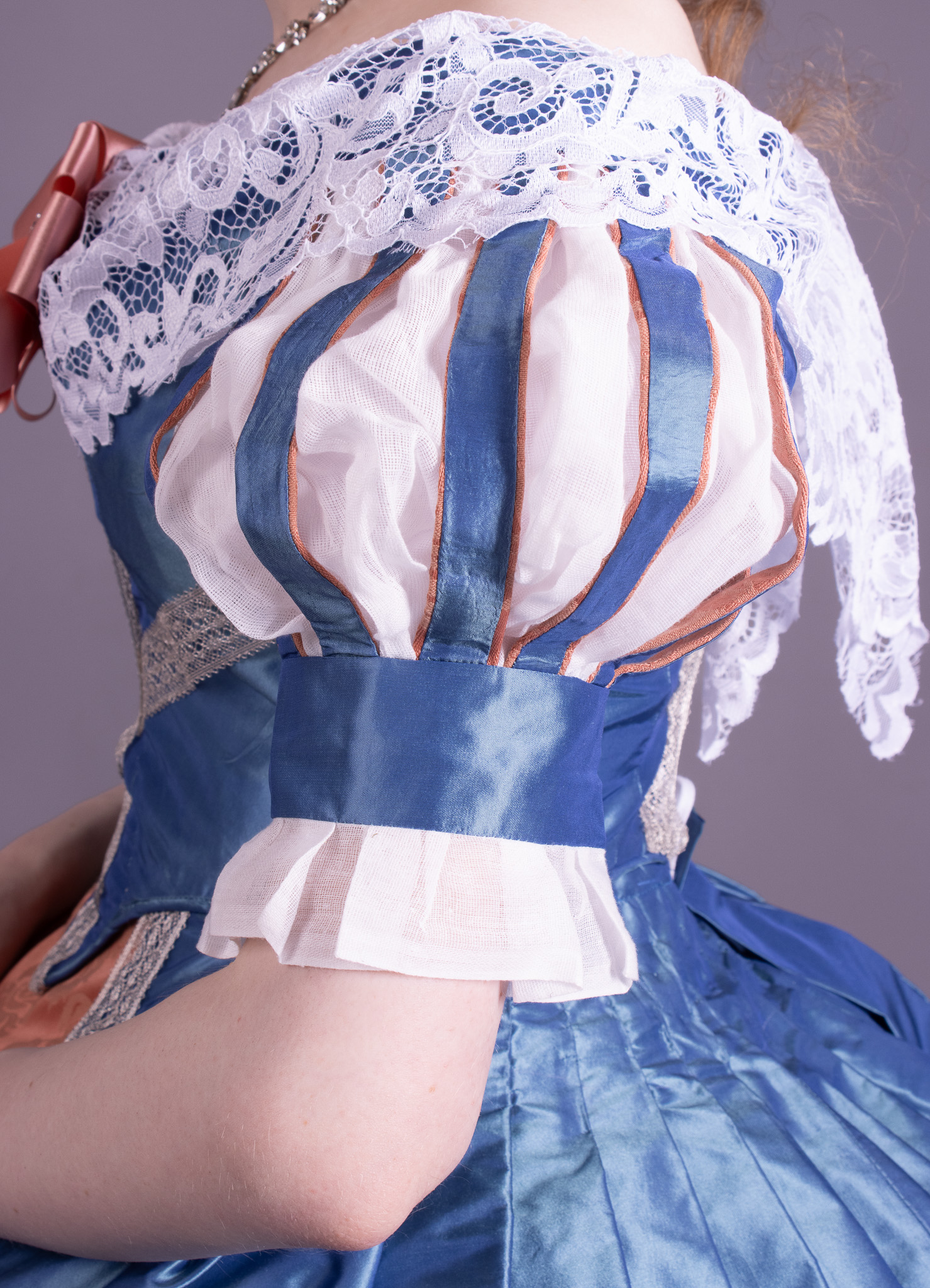 A blue-and-white costume dress with striped puff sleeves and white lace, shown from the back against a plain grey background.