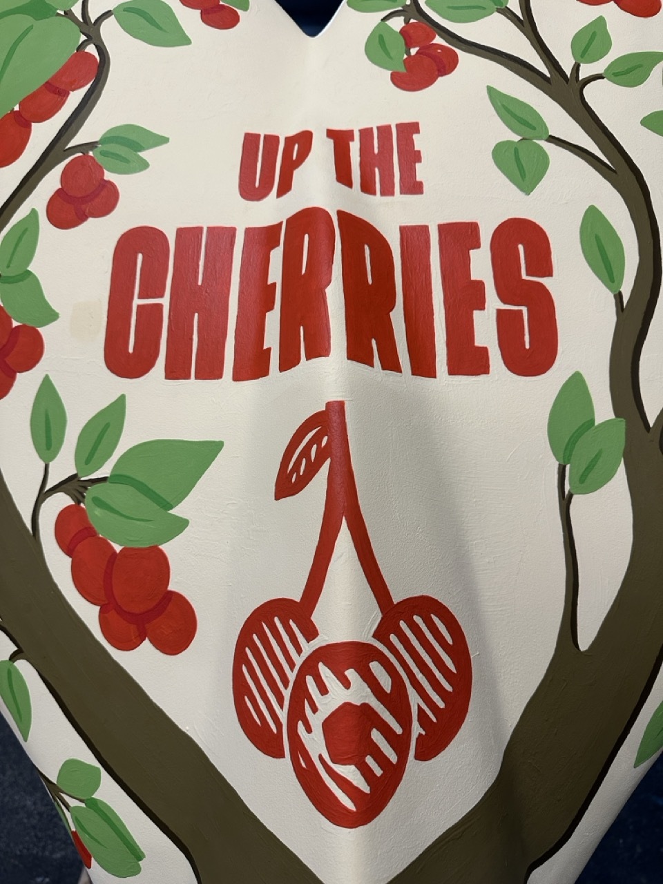 Close-up of L'Eisha's tail design, red text reading 'up the cherries' surrounded by cherries and tree branches with leaves.