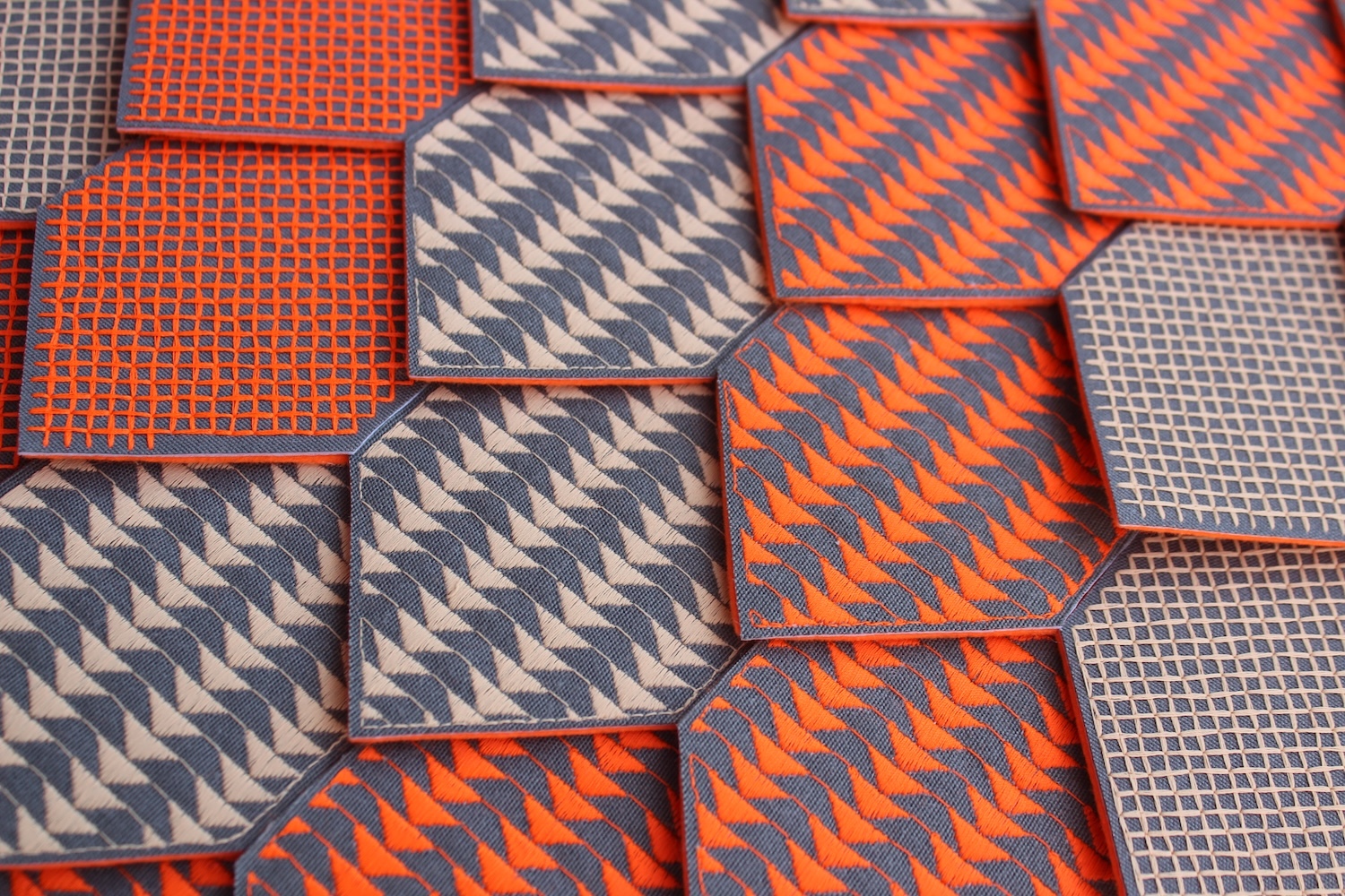 Collection of neckties with geometric patterns in orange, grey, and white featuring zigzags, checks, and diagonal stripes.