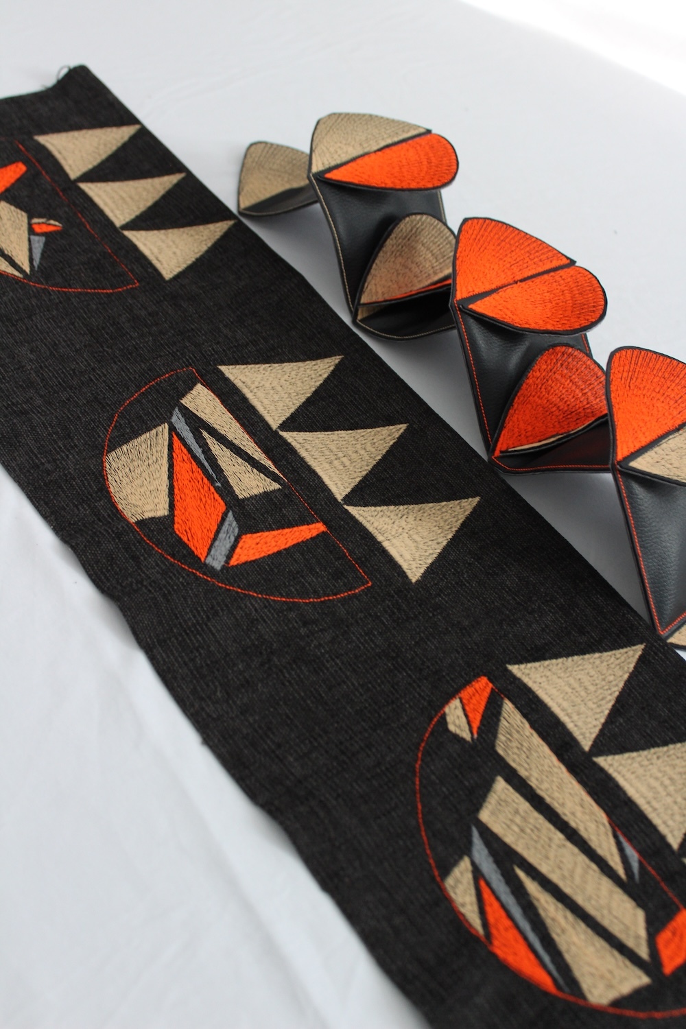 Black fabric with orange, beige and black geometric triangle patterns. Matching high heels with similar triangular design elements.