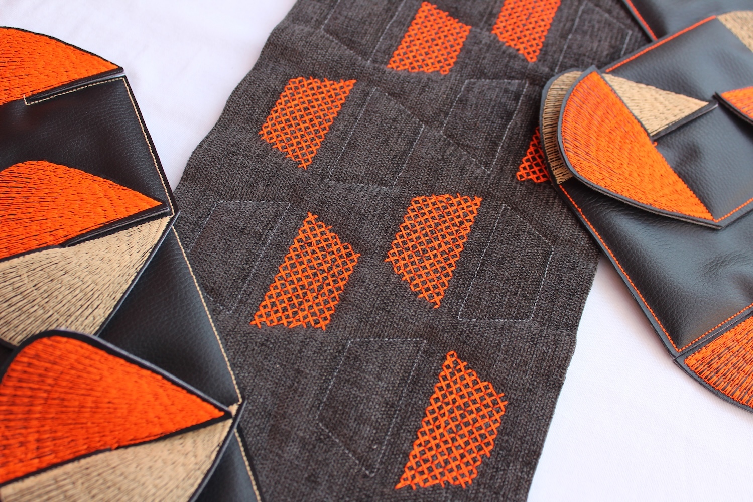Three geometric textile pieces with orange, grey, and cream patterns - hexagonal shapes on left, diamond grid in centre, curved forms on right.