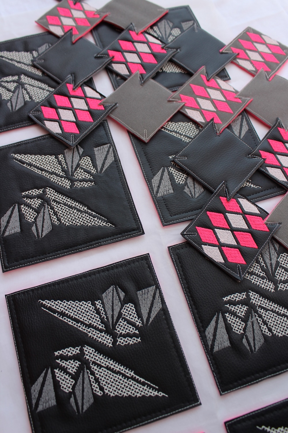 Multiple black fabric squares with geometric patterns in pink, white and grey arranged on white surface.