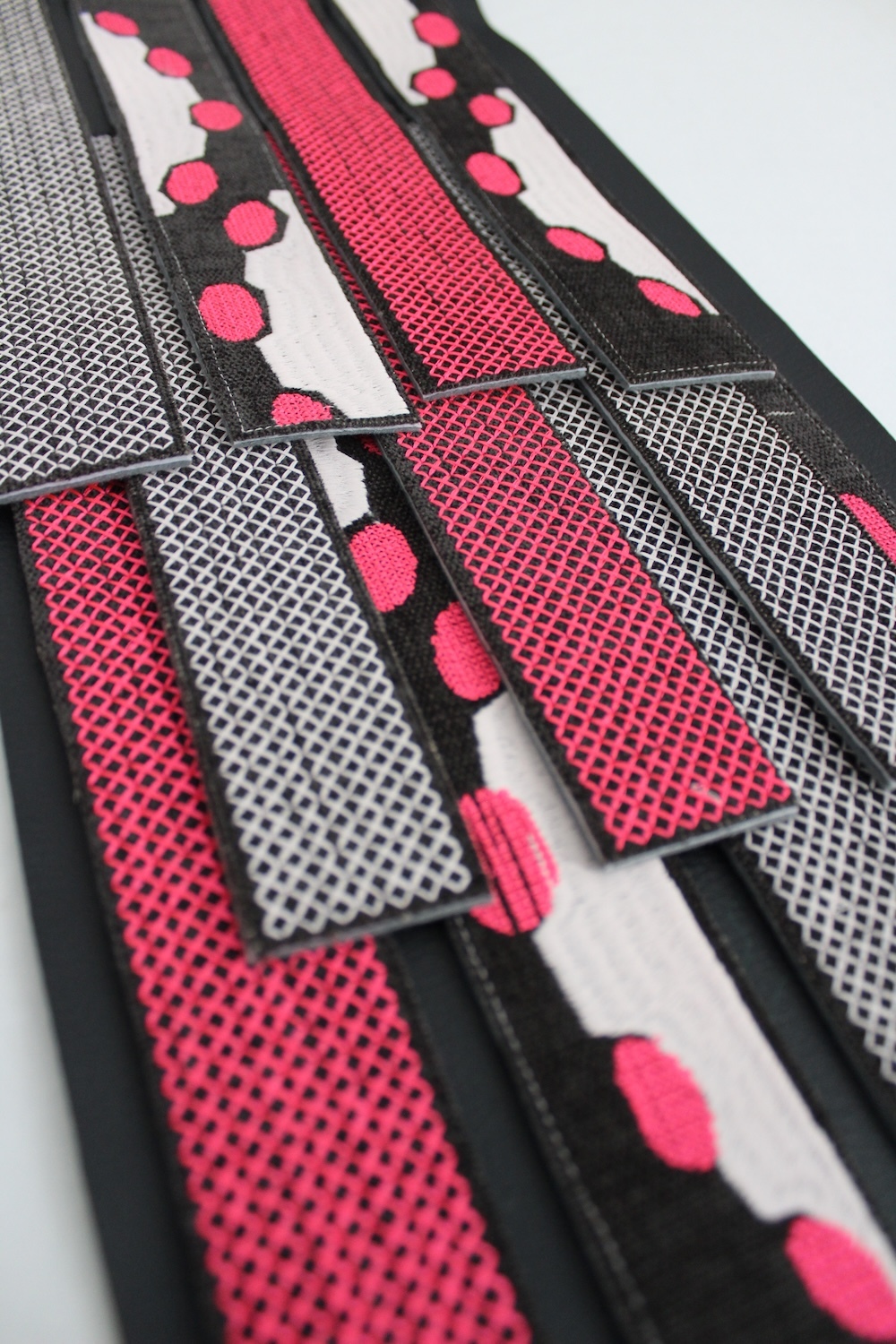 Fabric strips with pink polka dots, red mesh sections, and black trim arranged in geometric patchwork pattern.