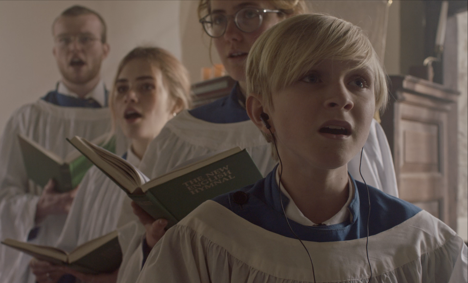 Blonde boy singing in a church choir wearing earphones.