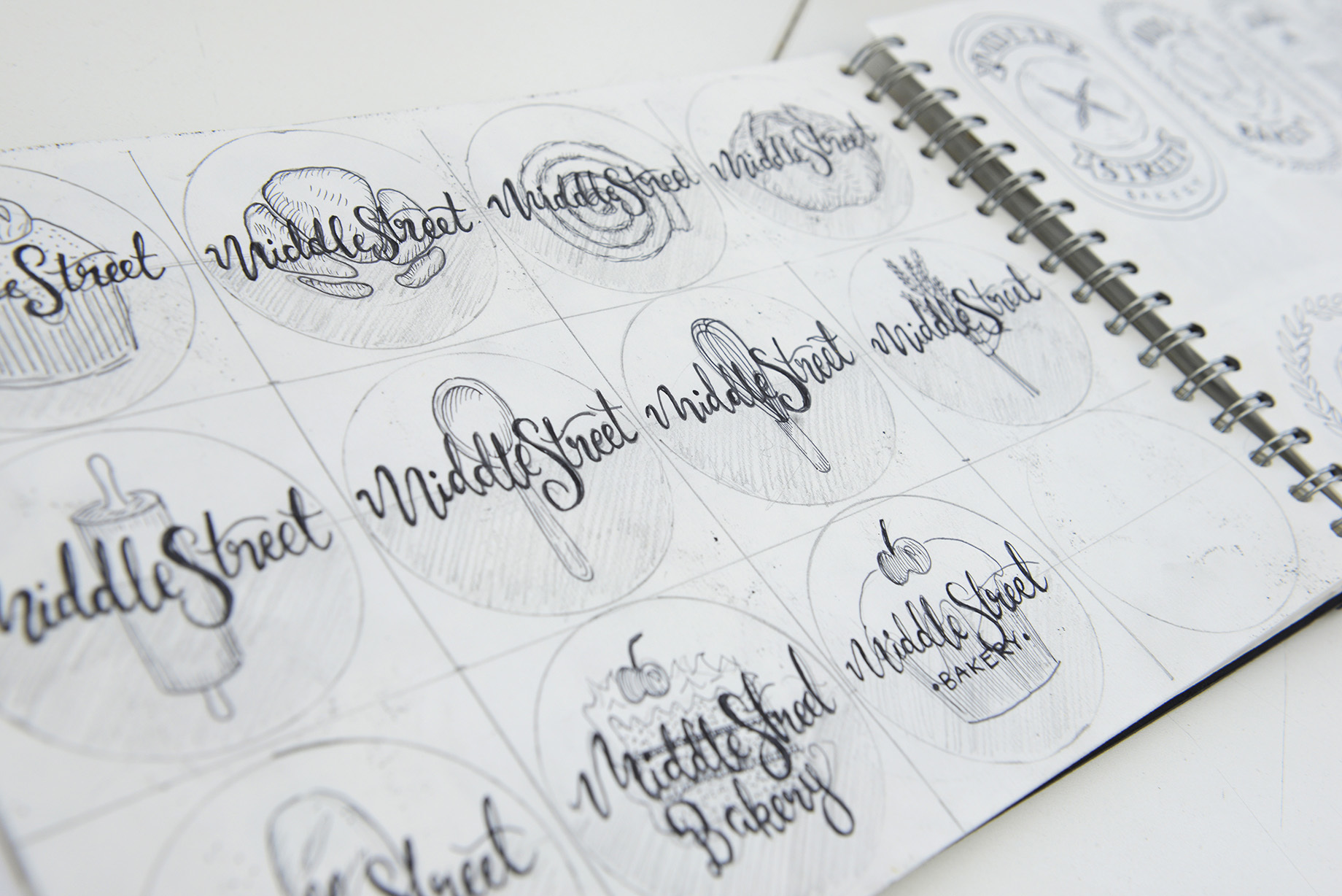 A sketchbook page with eleven different versions of a logo for Middle Street Bakery.