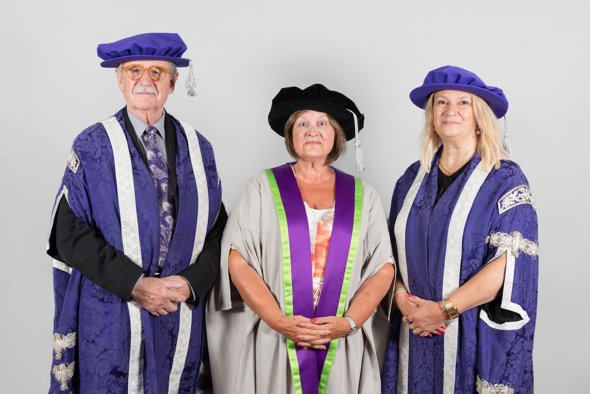 Professor Sir C. Frayling, E. McBain and L. Mann, in academic graduation robes and caps - two in purple and blue gowns with matching caps, one in grey gown with black cap.