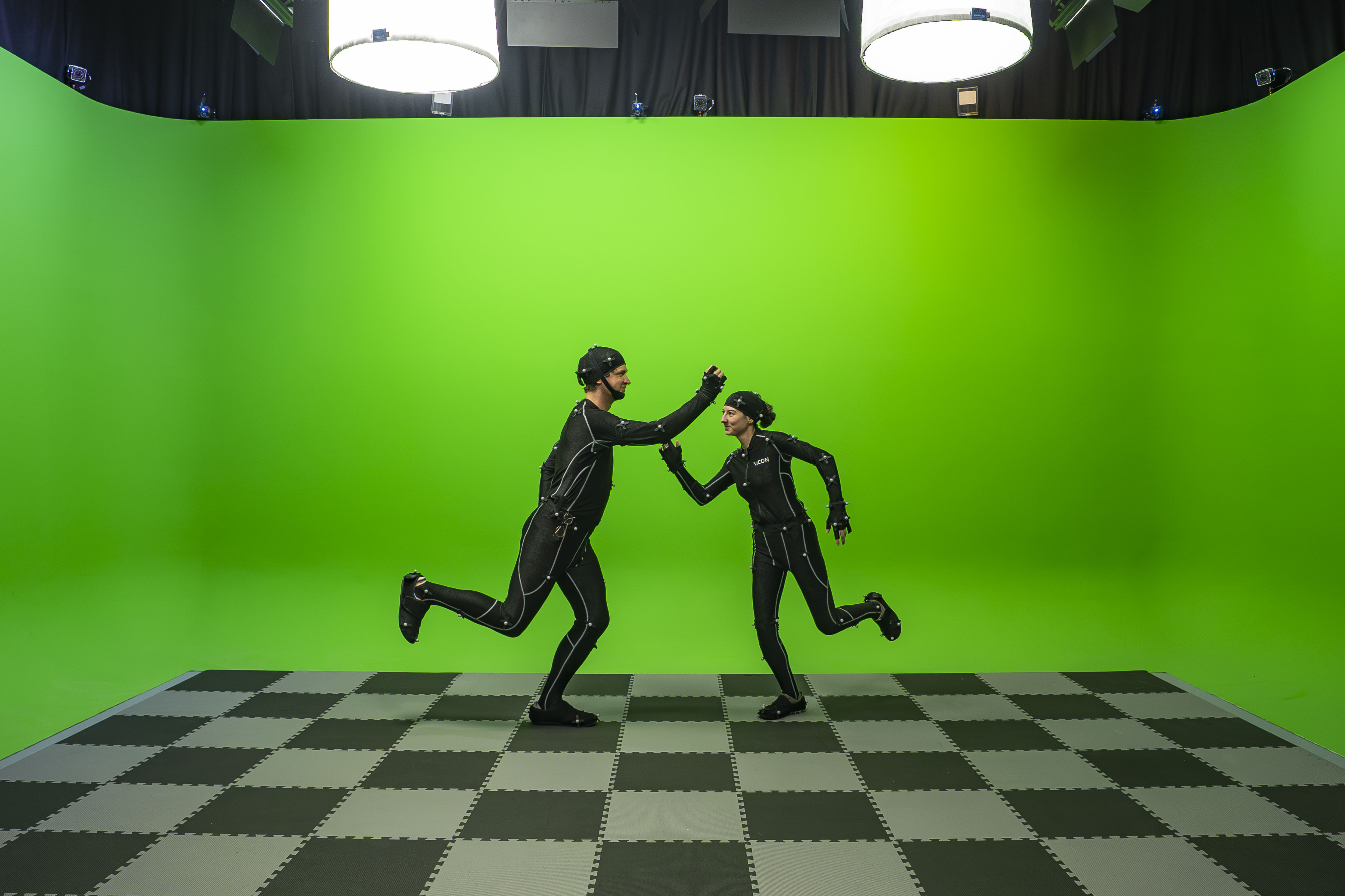 Two people wearing motion capture suits facing one another and posing in front of a Chroma-Key green surround.