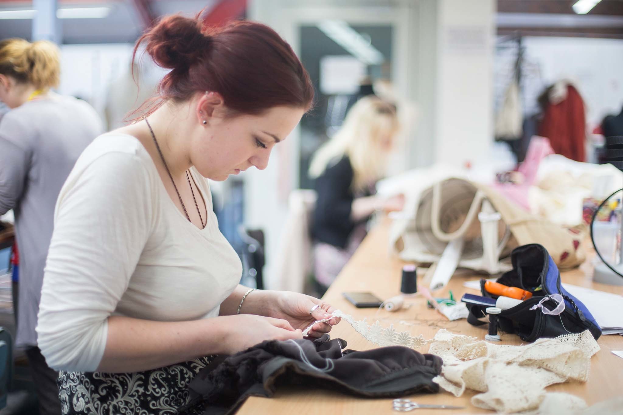 A person sits a table and works with a fabric trim.