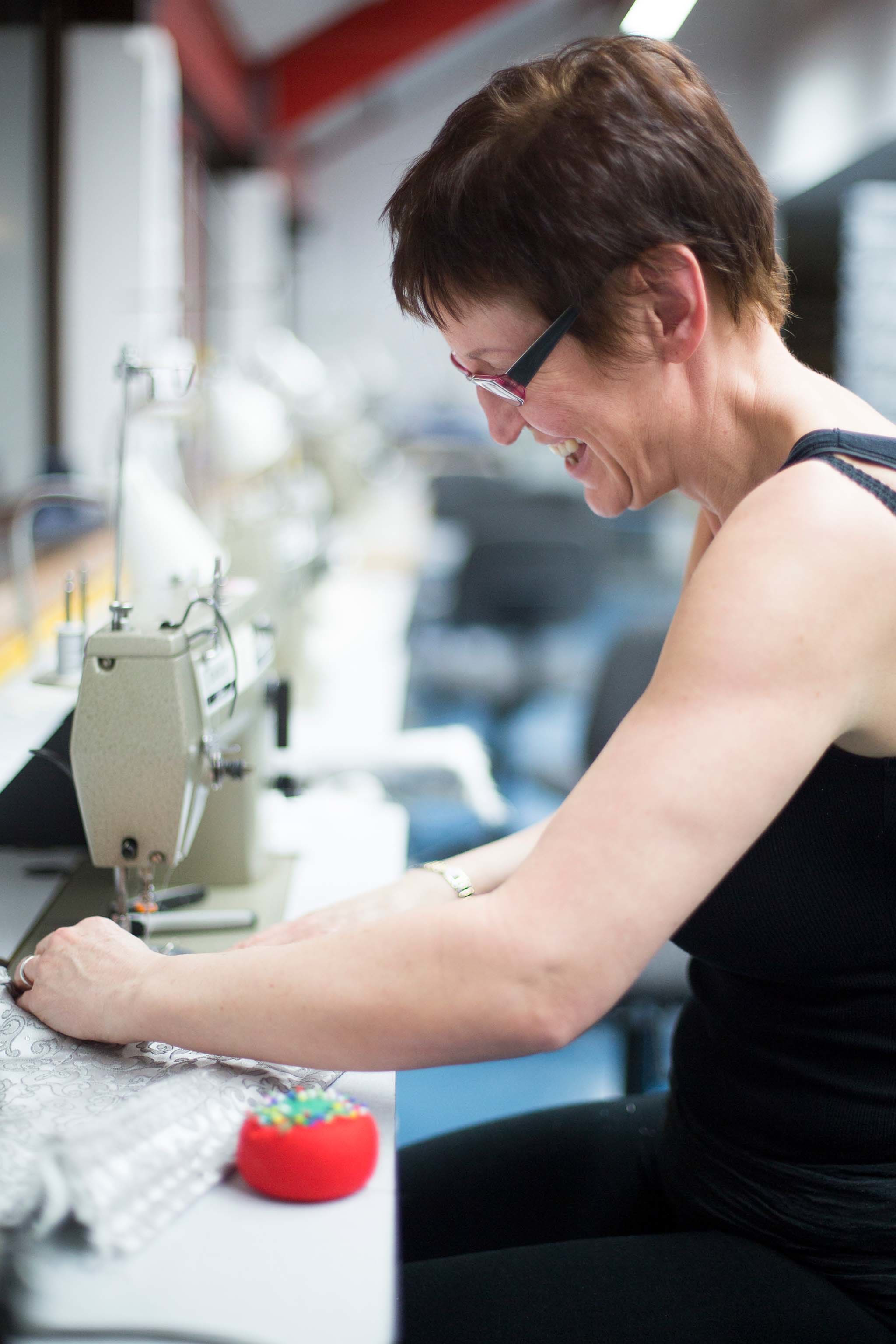 A person smiles and sits working at a sewing machine.