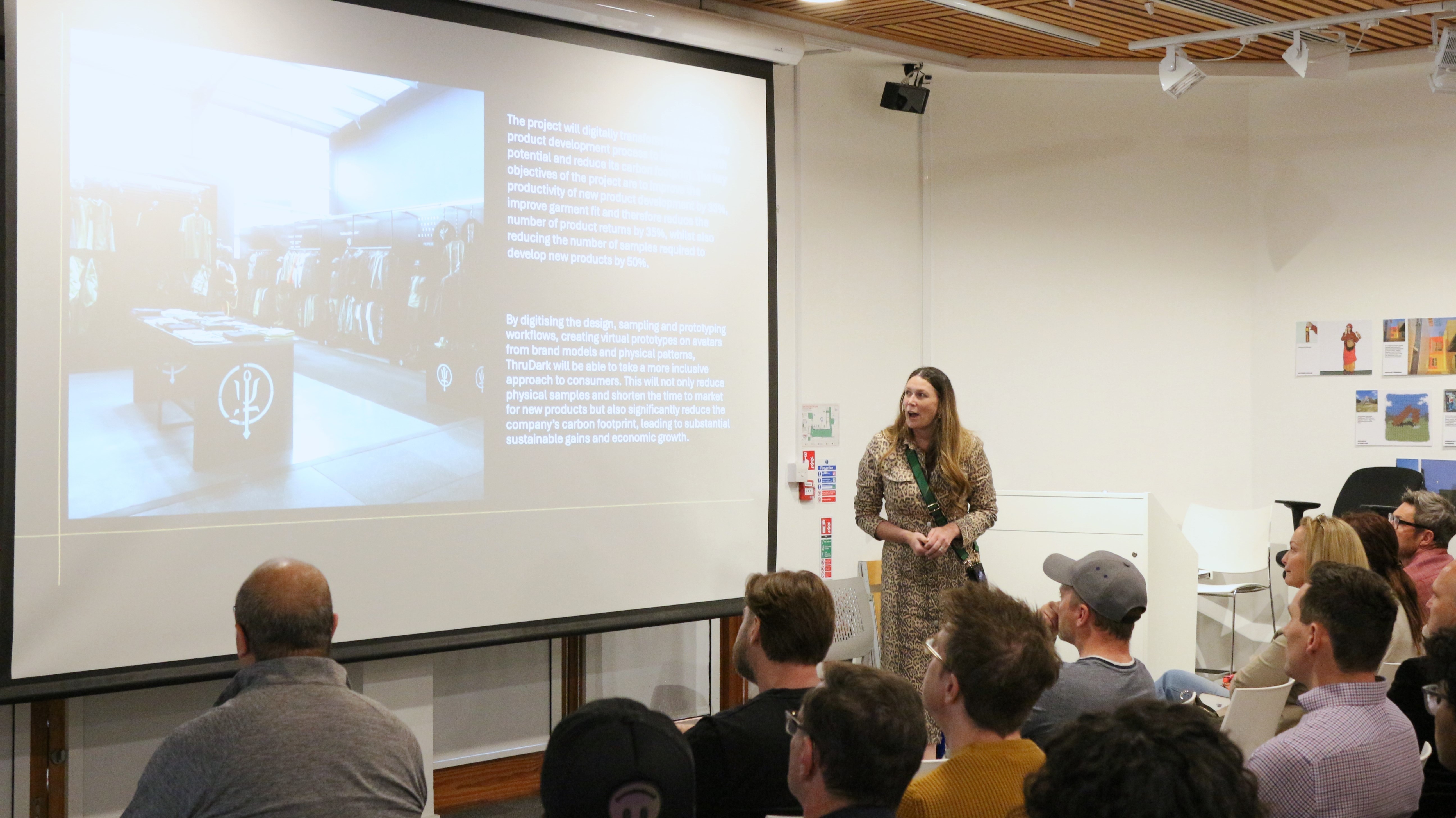Dr P Norman speaking to an audience in a lecture hall, in front of a large screen showing a presentation slide.