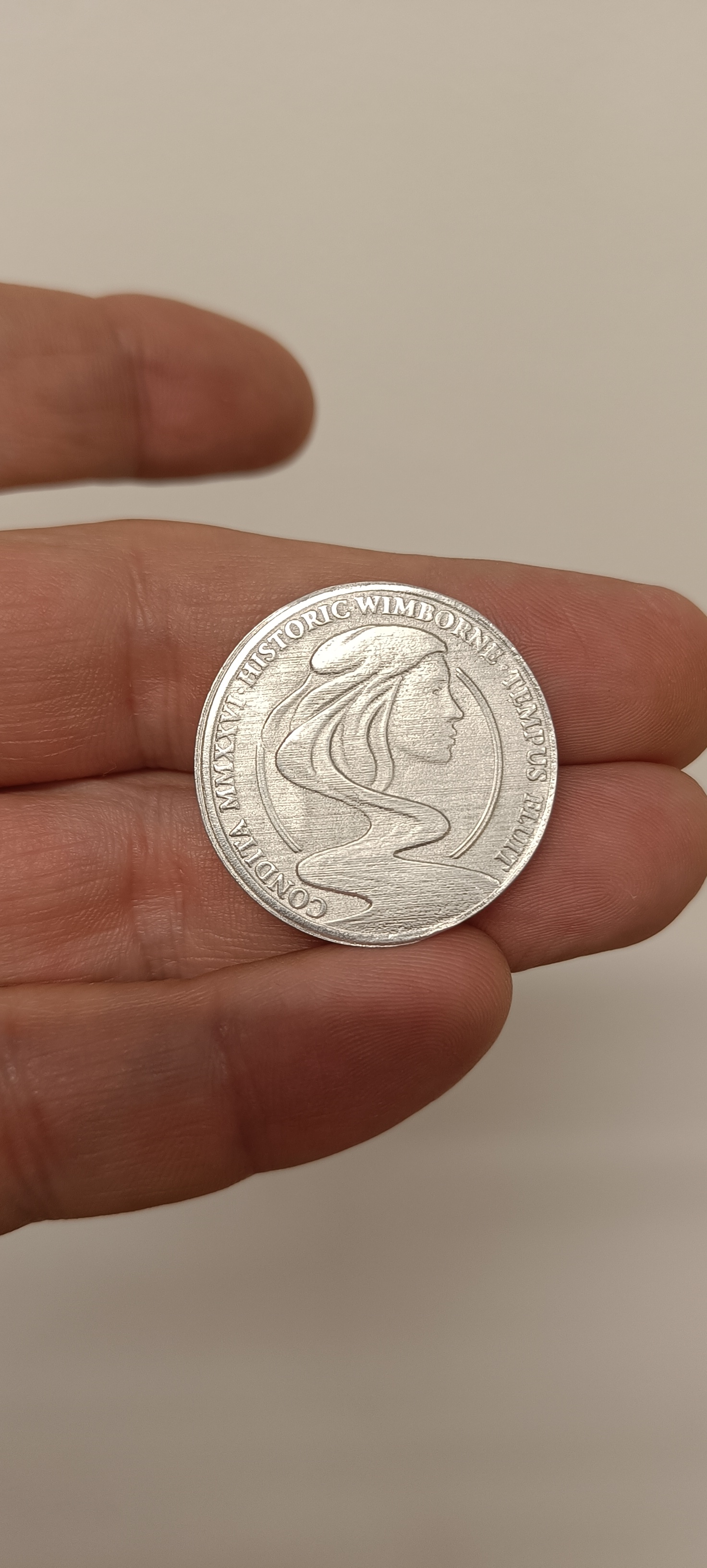 A silver Roman-style coin lying on a person's fingers.