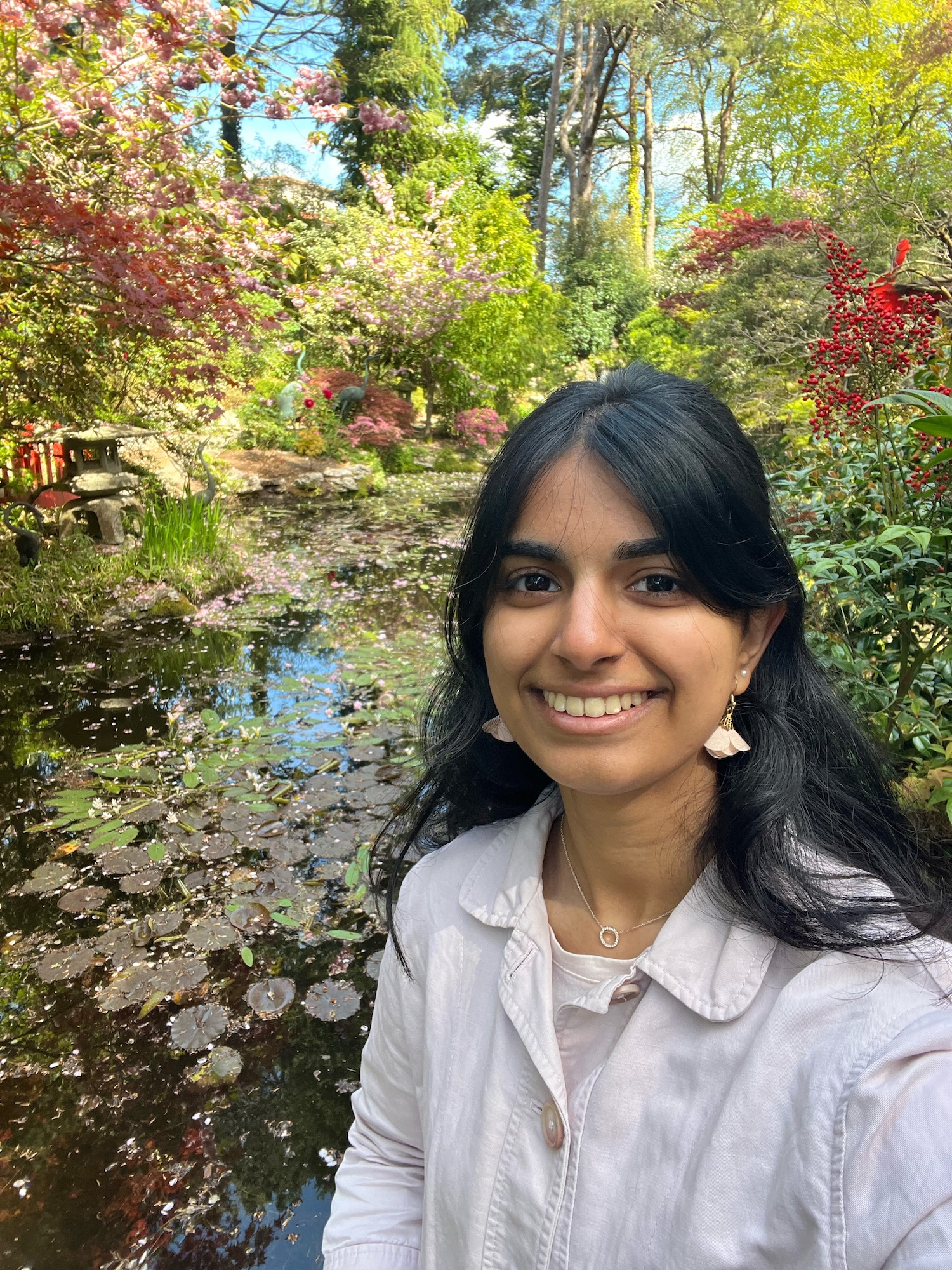 BA (Hons) Interior Architecture and Design student J Gajjar poses for a selfie with a pond and greenery in the Japanese Garden at Compton Acres, Dorset, in the background.