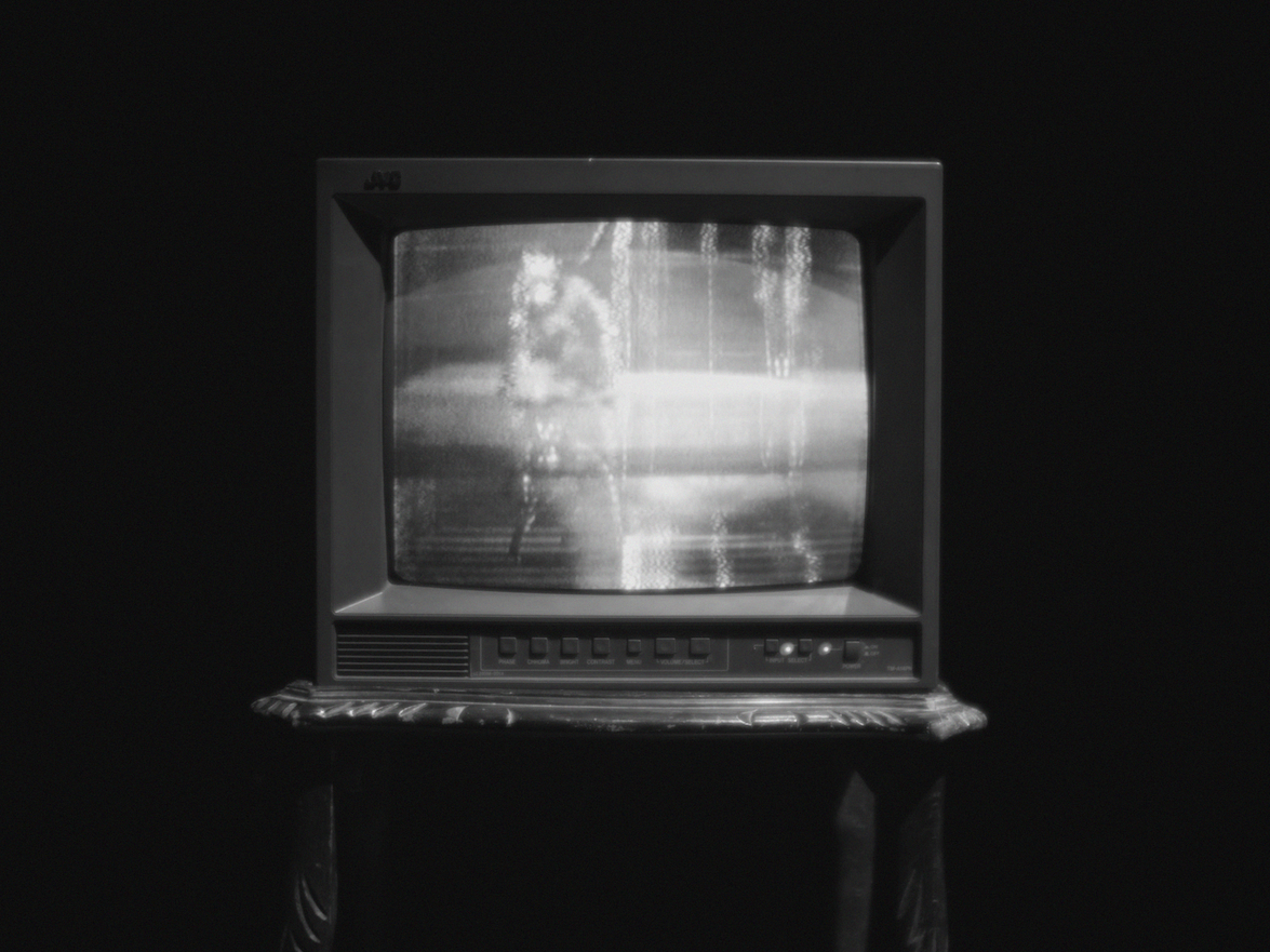 Vintage CRT television on wooden stand displaying grainy black and white image, photographed against dark background.
