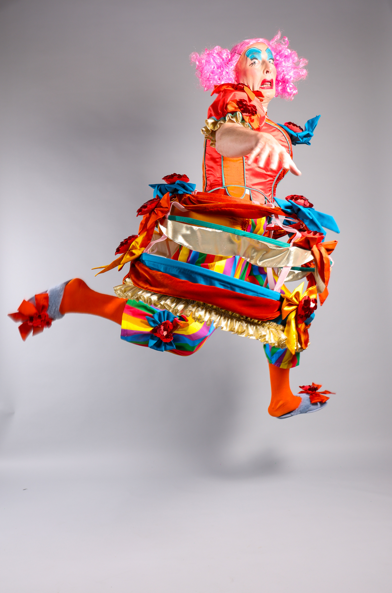 A performer in pantomime dame-style costume and make-up, pictured while leaping.
