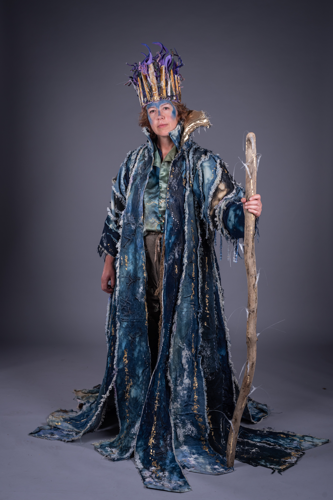 A model poses for a photo while dressed in a long druid-style costume and headdress, holding a staff.