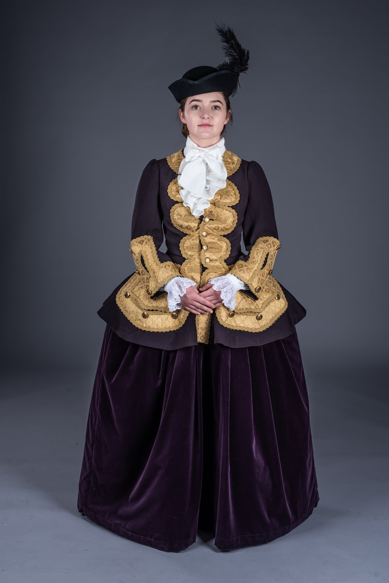 A model poses for a photo in a period-style riding habit and headdress.