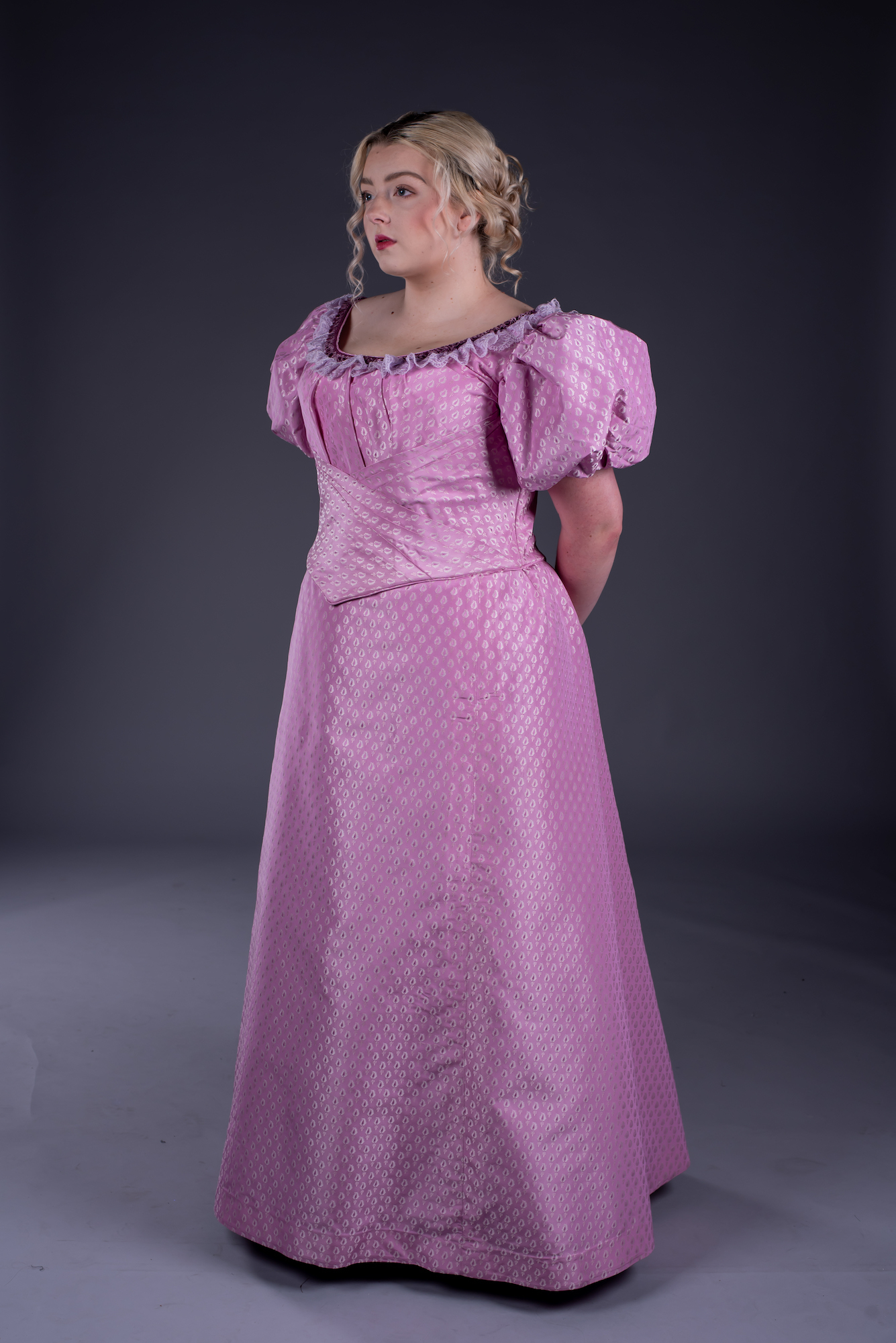 A model poses for a photo while wearing a pink period-style costume.