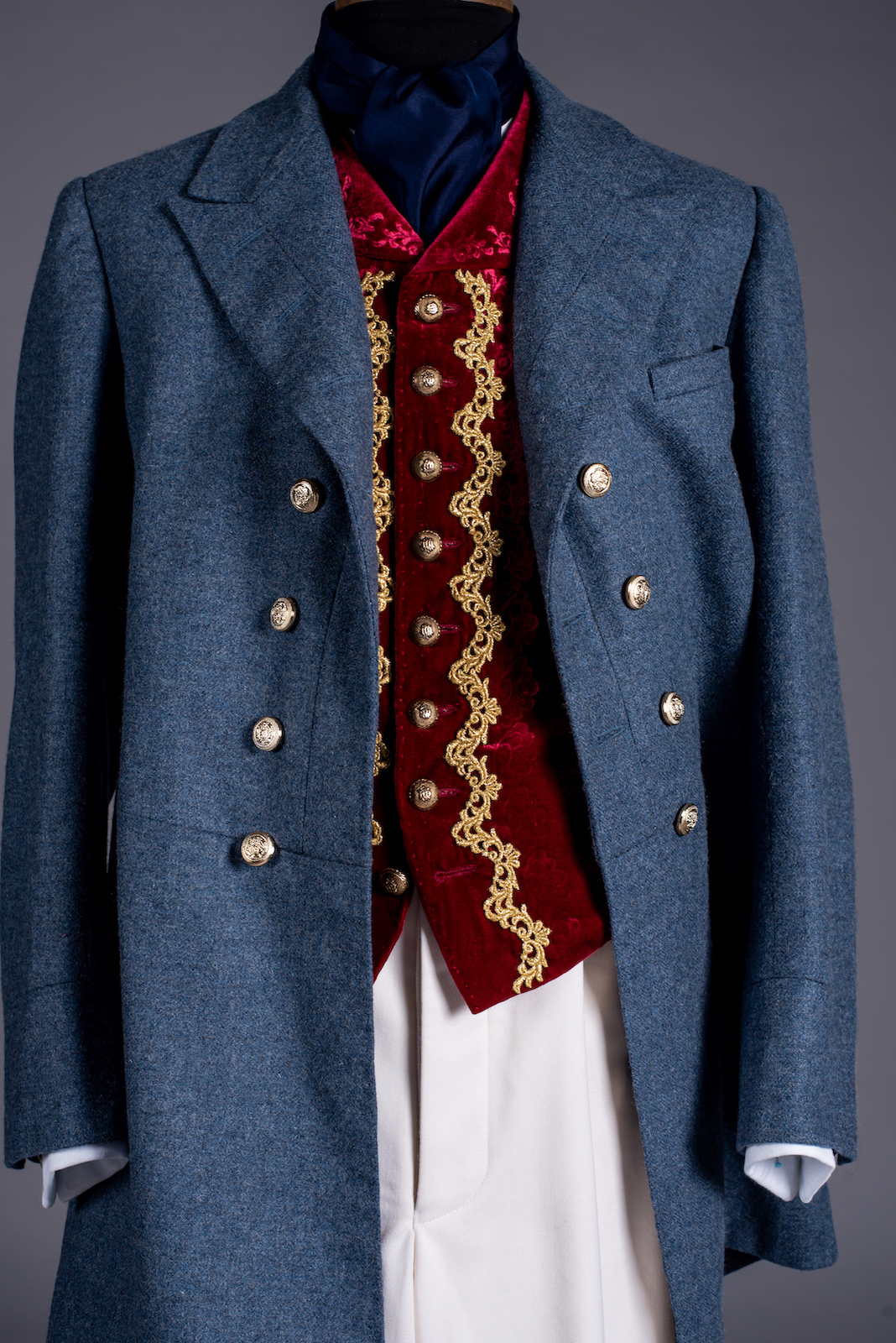 Close-up of a long men's jacket with a red and gold waistcoat underneath, on a mannequin.