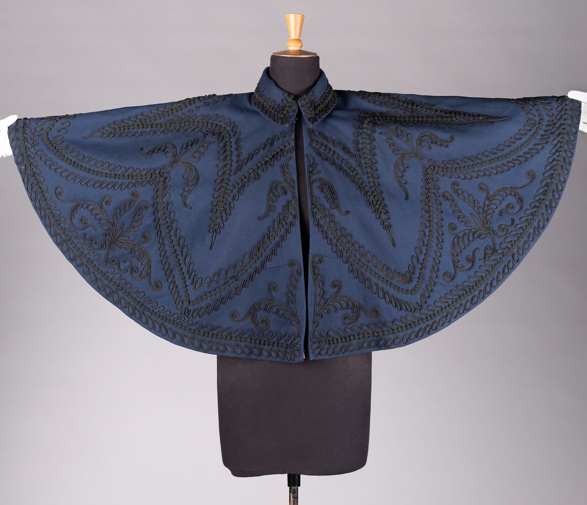 A blue late-Victorian woollen cape with black silk lining, open and displayed on a black mannequin.