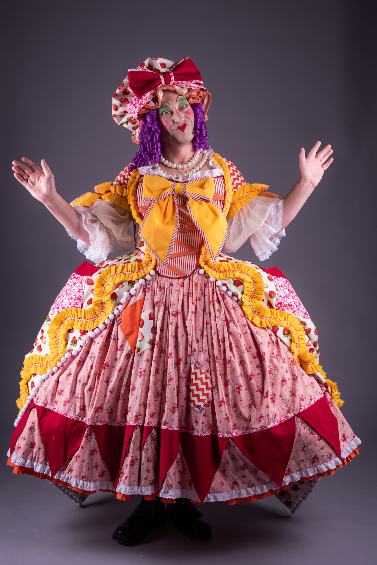 A model poses for a photo wearing a pantomime dame-style dress and bonnet.