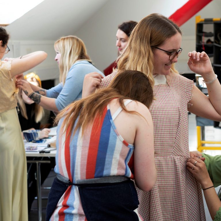 A group of people standing in a costume studio in the middle of a costume fitting session.