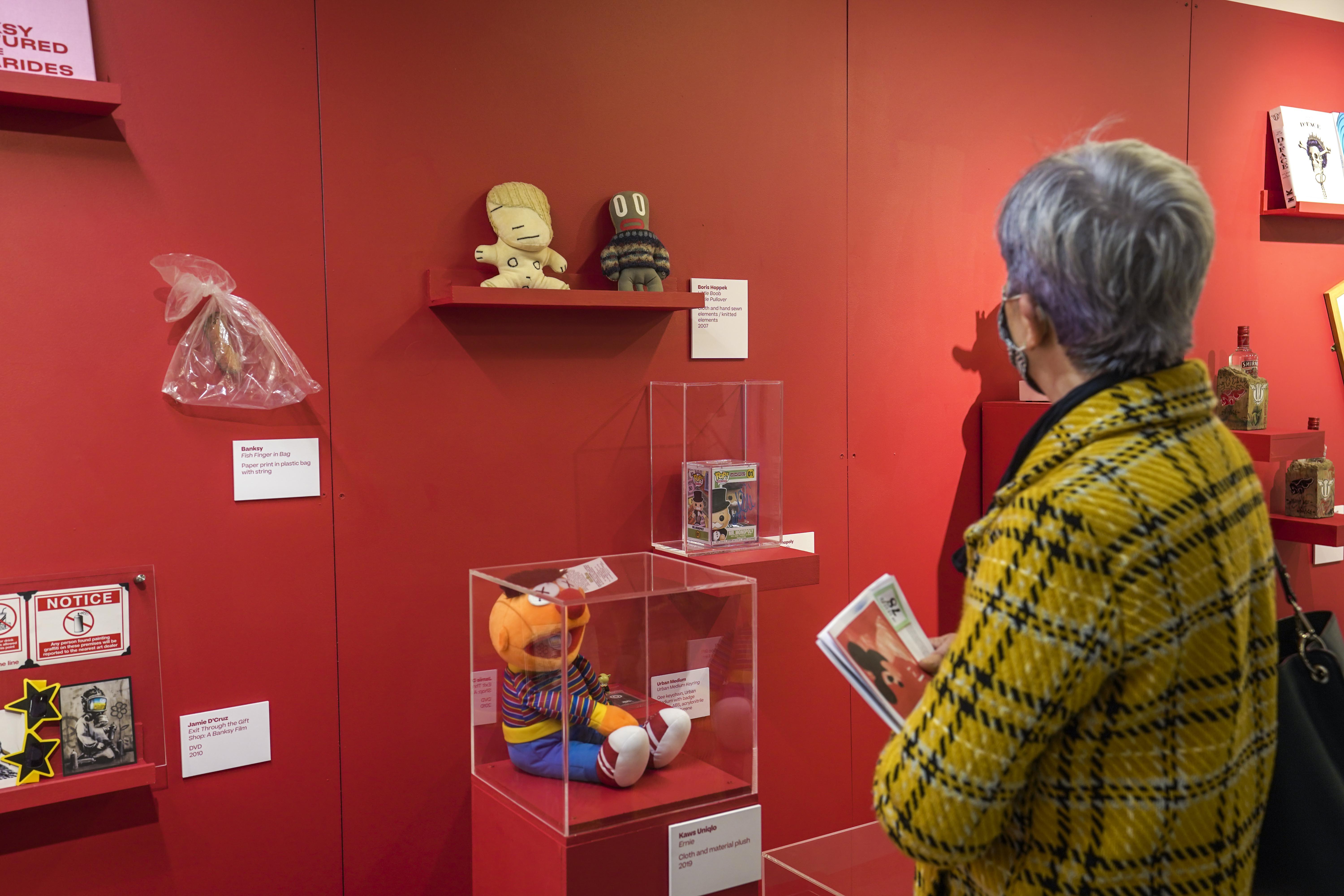 A set of children's toys on display on shelves and in cases as part of an exhibition. A person is shown looking at them.