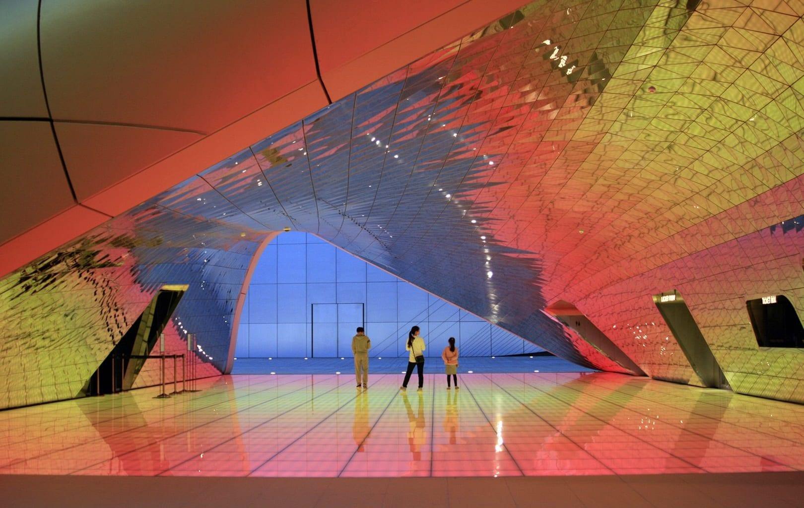 Three people stand in a wide open lobby space, which has sloping ceilings and colourful lighting