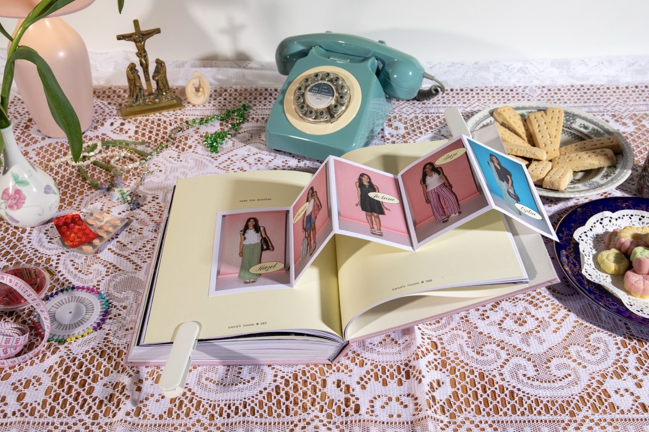 Open photo album with pop-up images, vintage turquoise rotary telephone, white lace tablecloth, plant, and decorative items arranged on table.