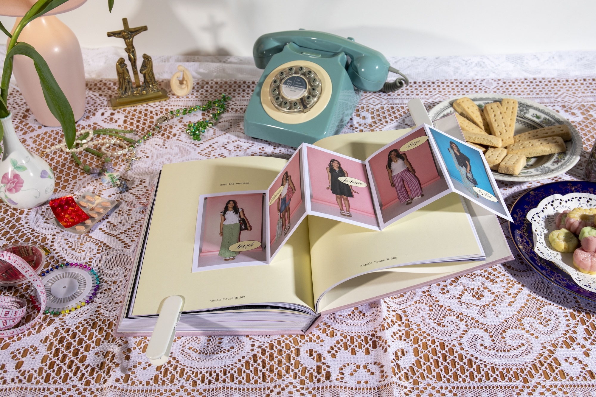 A table spread with a lace tablecloth and a copy of the book "Nana's House" by D Saldanha open to a fold-out of photos.