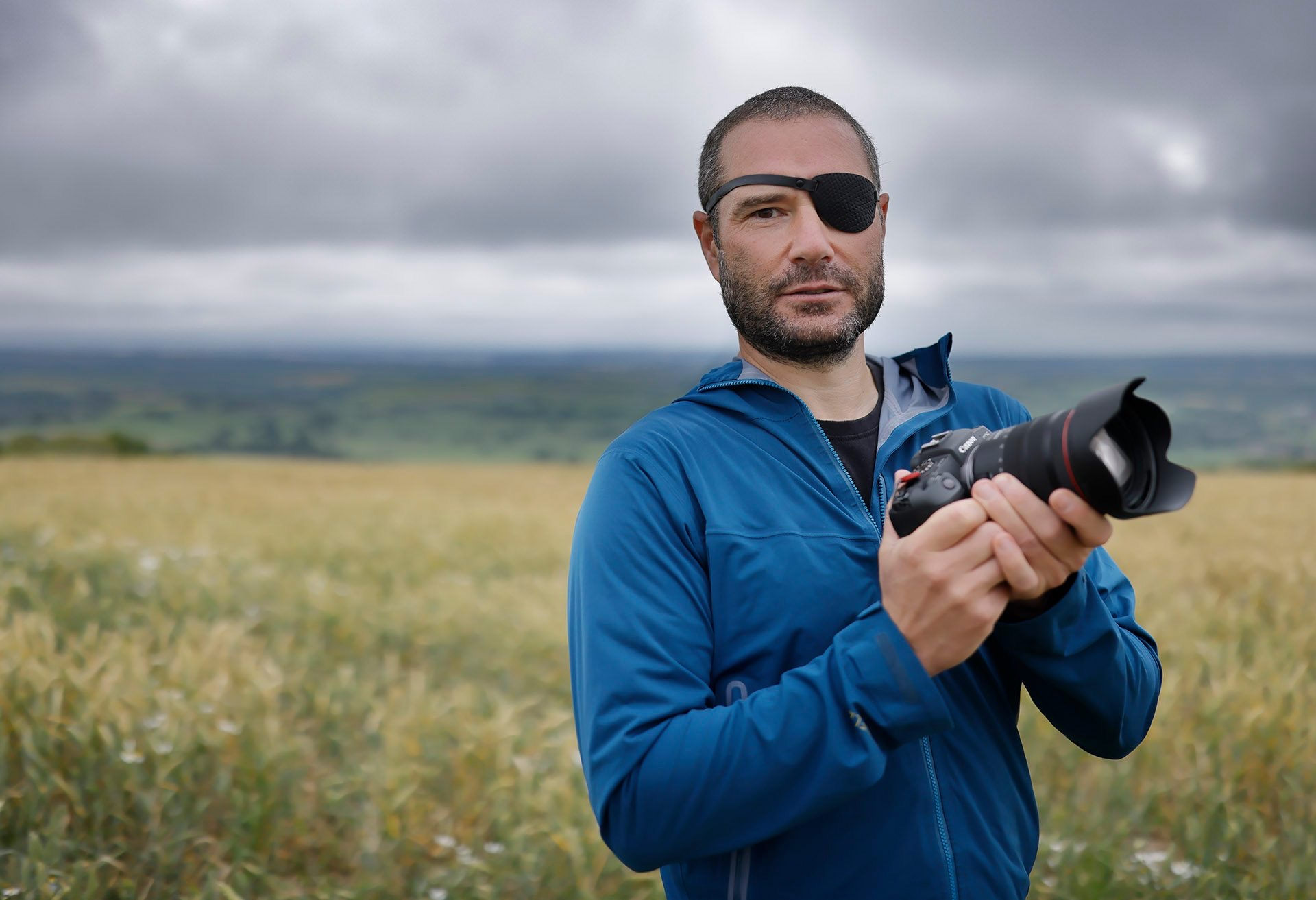 AUB Commercial Photography student David Baker standing with a camera in both hands, and grassland in the background.