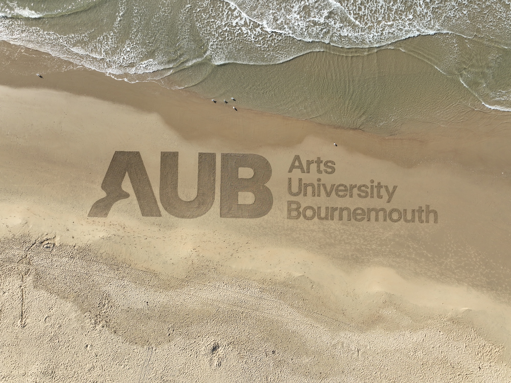 Overhead shot of the new AUB logo drawn in the sand at Bournemouth Beach.