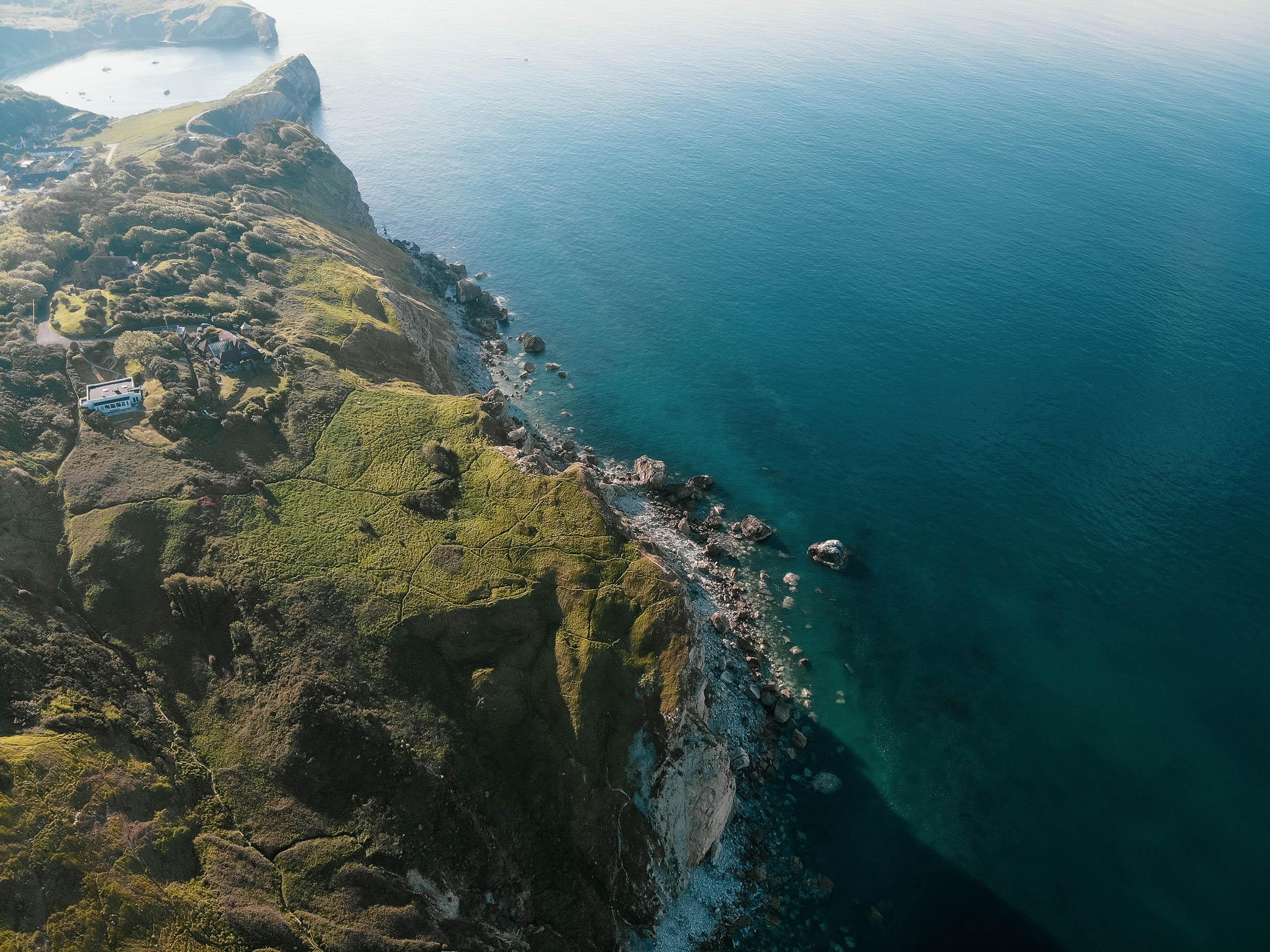 Aerial photo showing a mass of green headland on the left, cliffs and the sea beyond towards the centre and right.