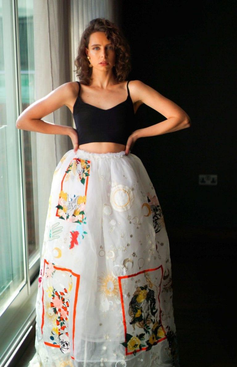 A model in costume poses for a photo by a window with their hands on their hips.