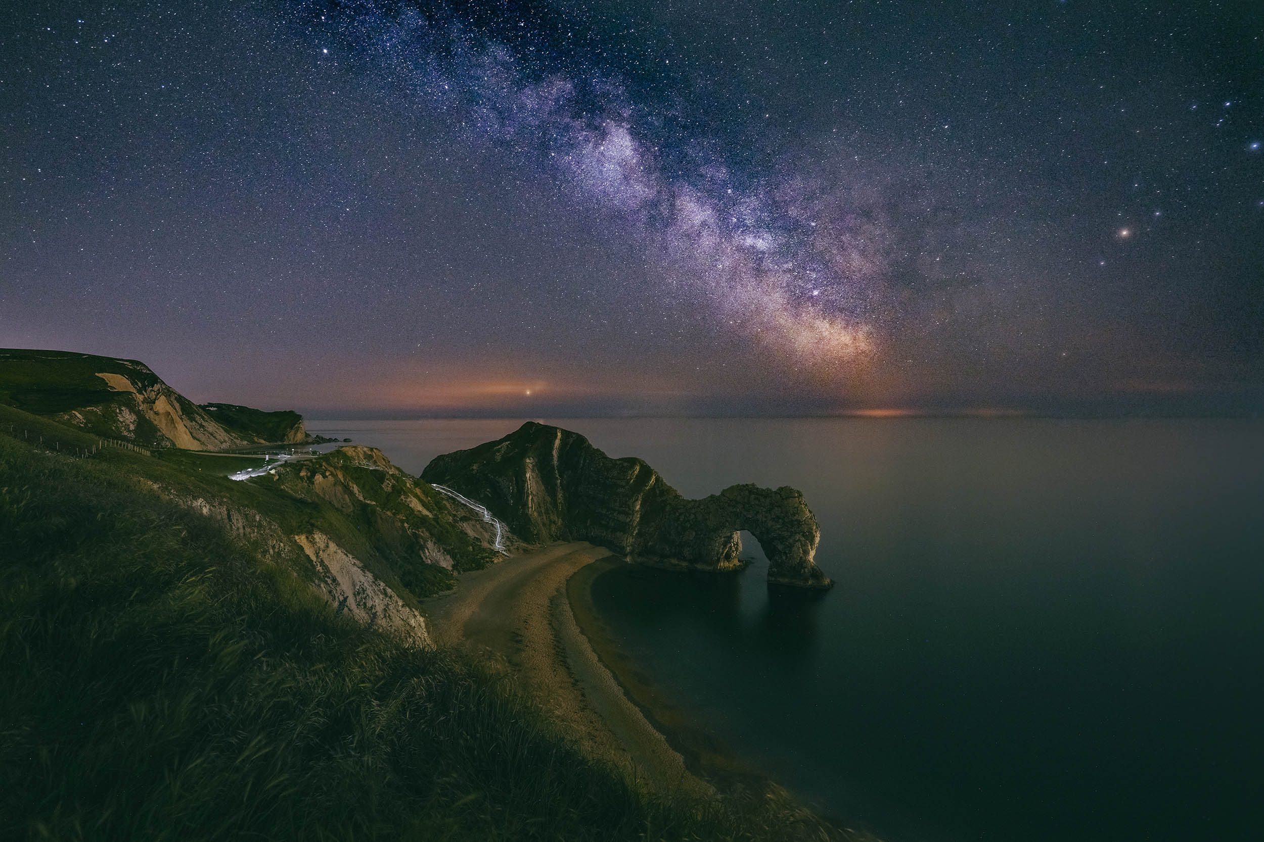 Long exposure of Durdle Door at night with a starry sky and the sea in the background.