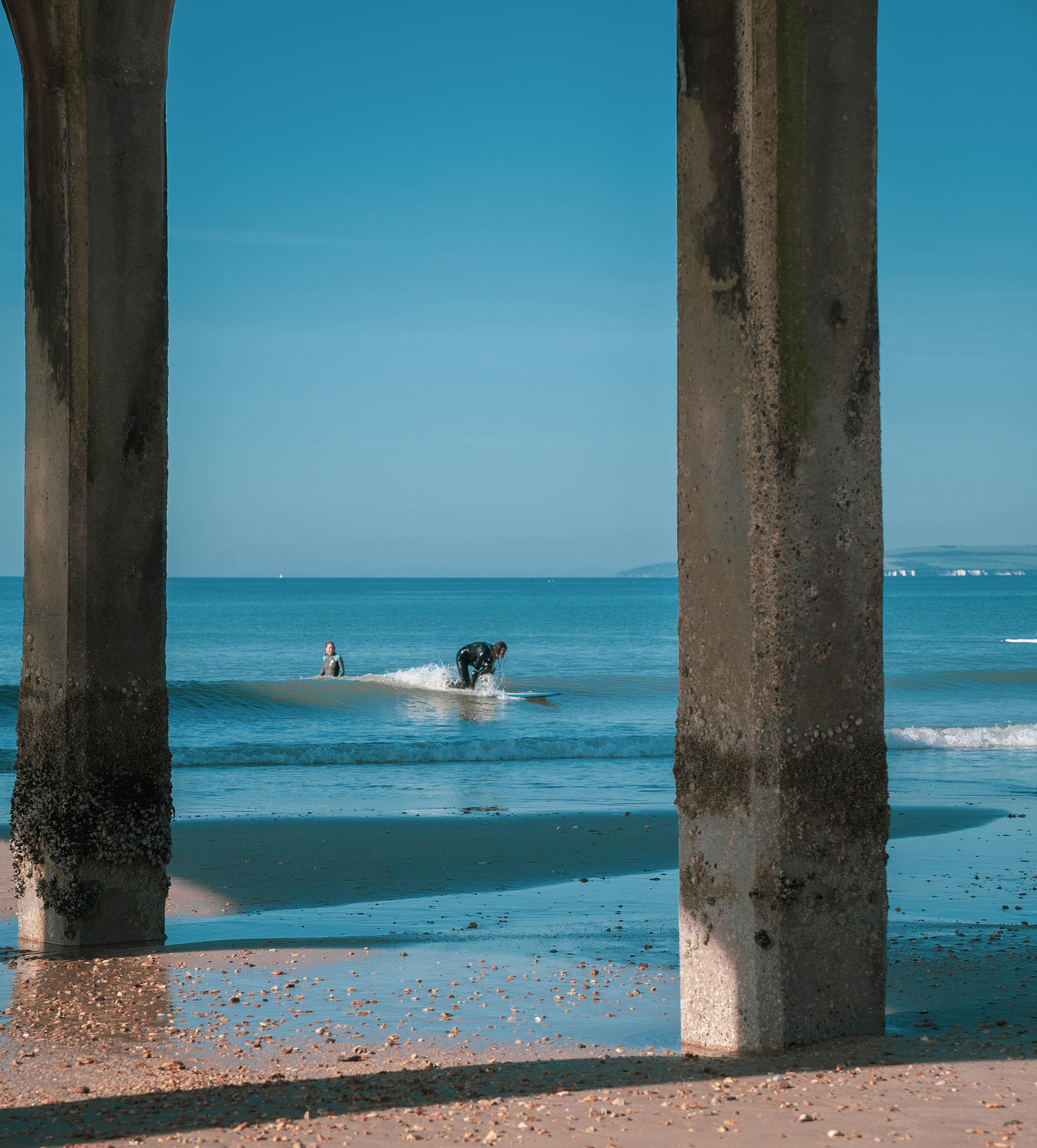 A surfer riding a wave. Two stone pillars are in the foreground.