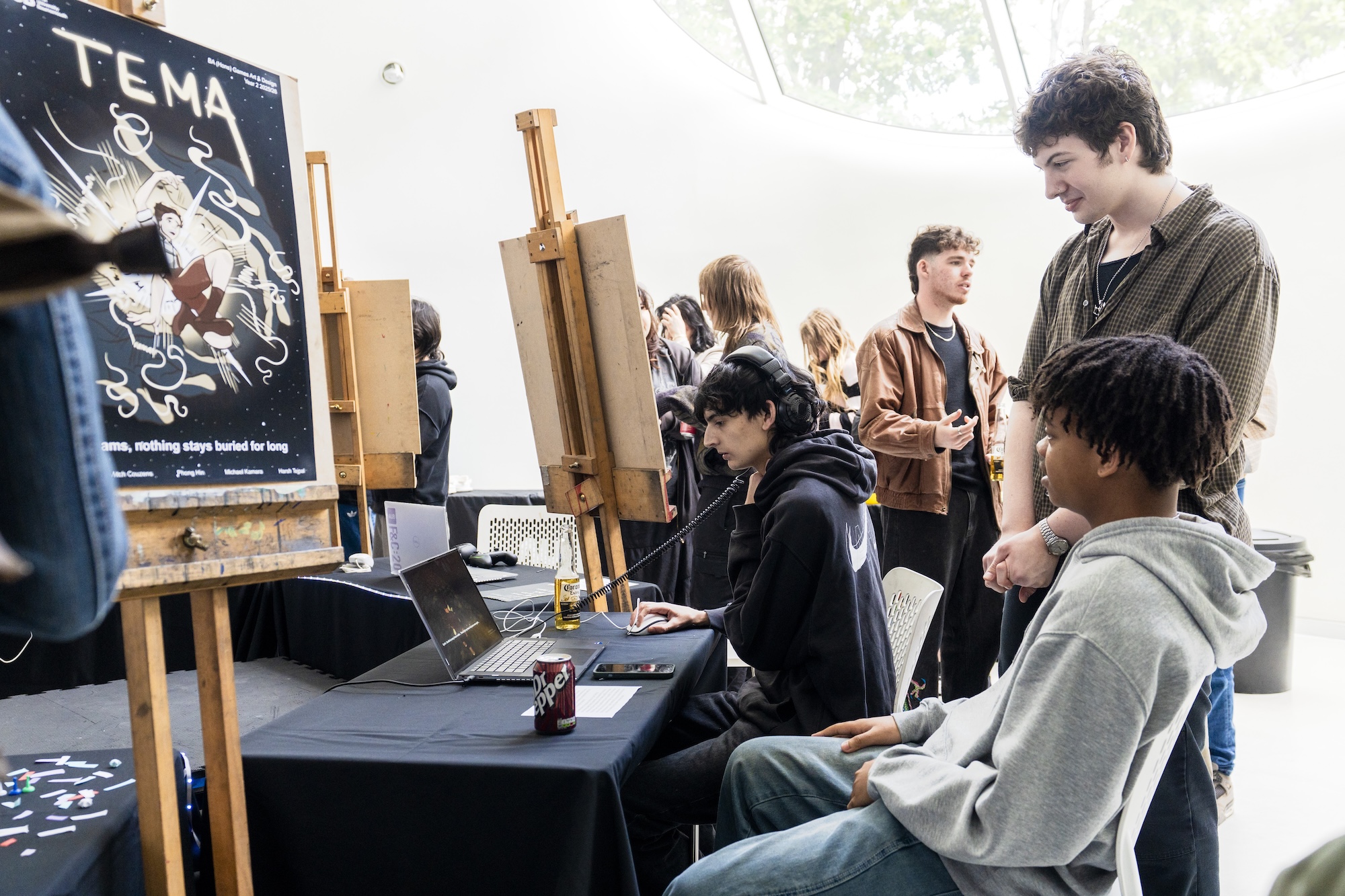 BA (Hons) Games Art and Design students sitting at a table playing a game called "TEMA" on a laptop in front of them.